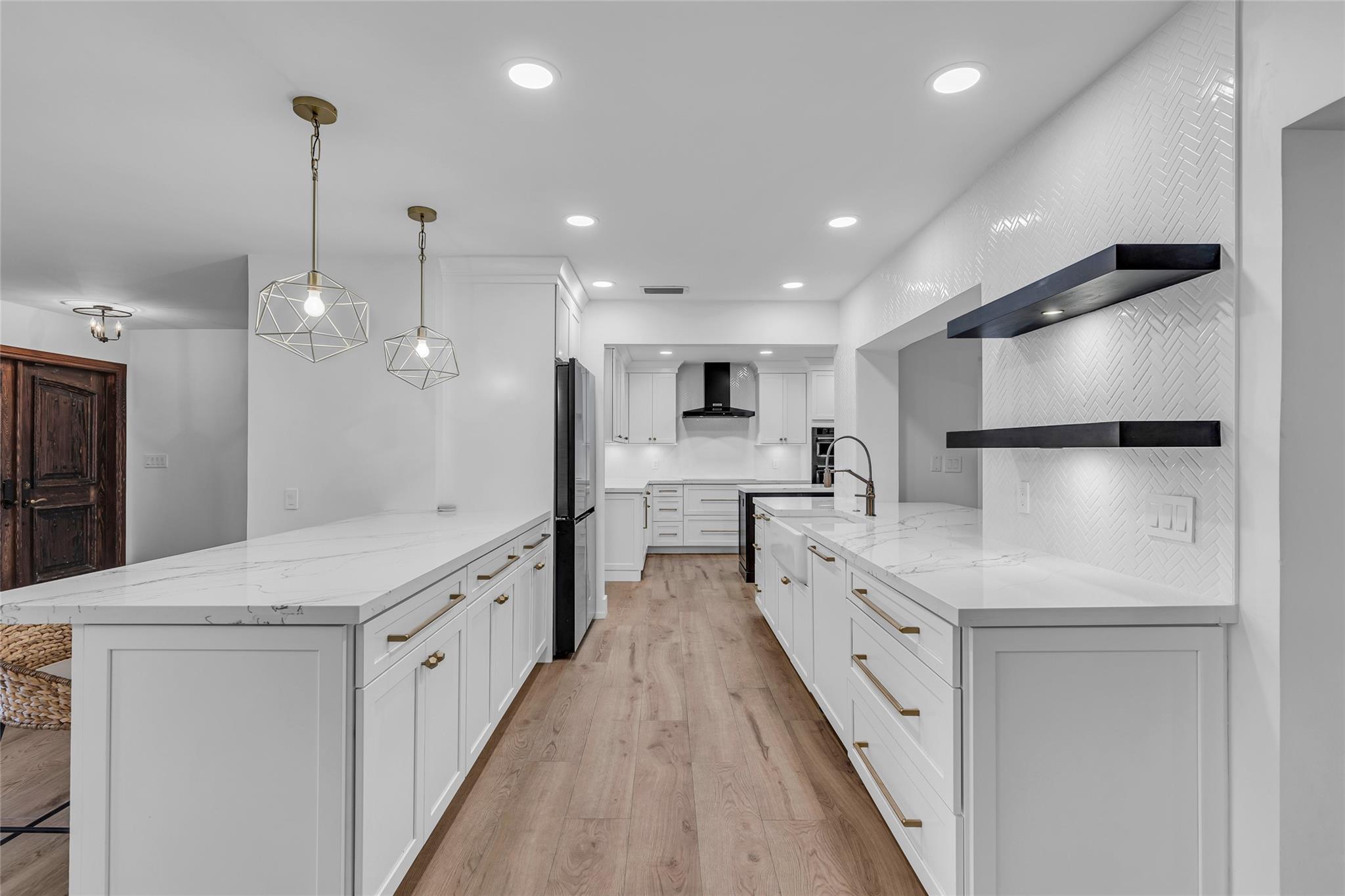 Kitchen is open into living room with white cabinets, quartz counters, tile backsplash and floating shelves