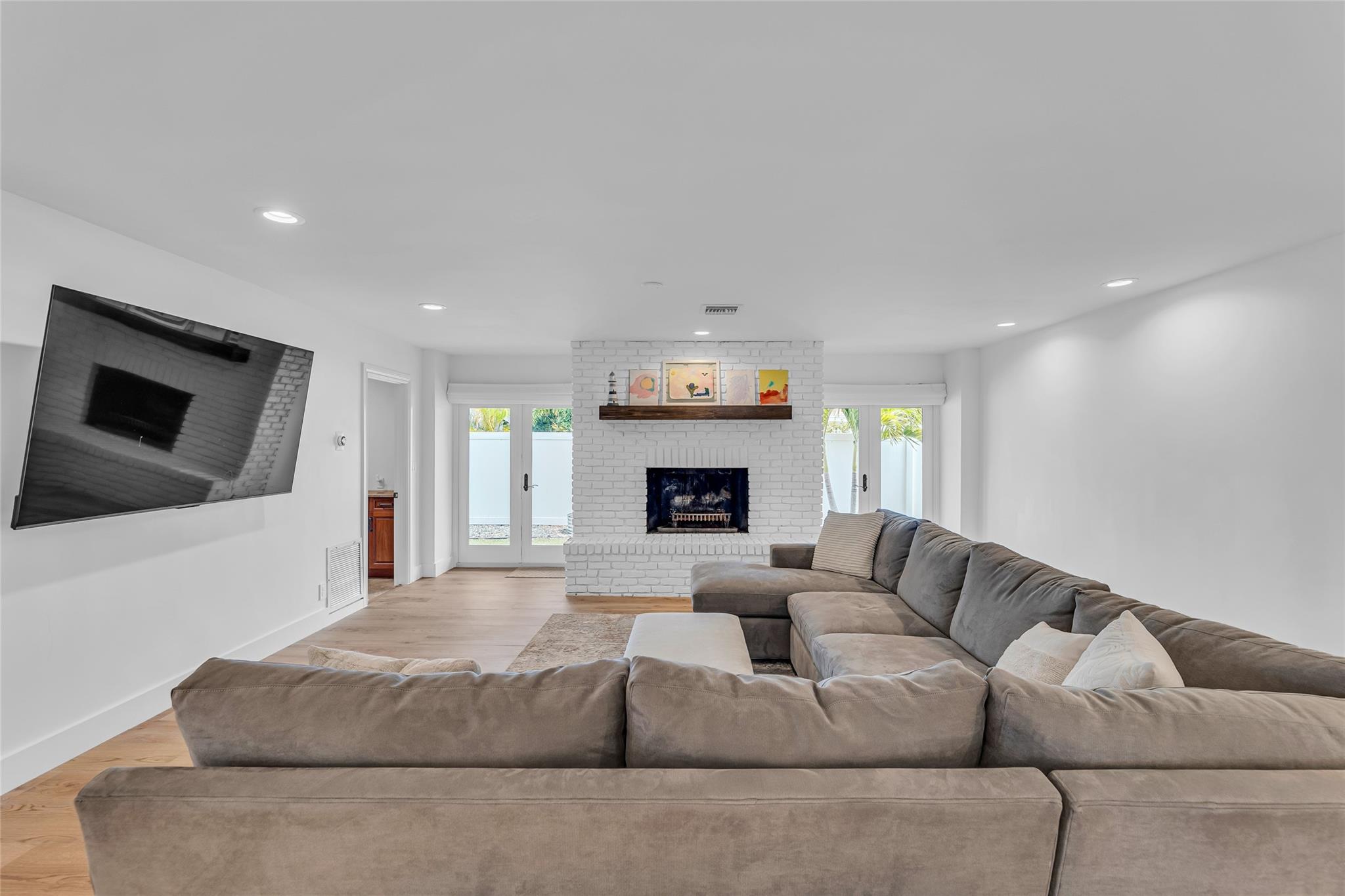 Large and spacious family room with a wood burning fireplace  with wood mantle and French doors out to backyard