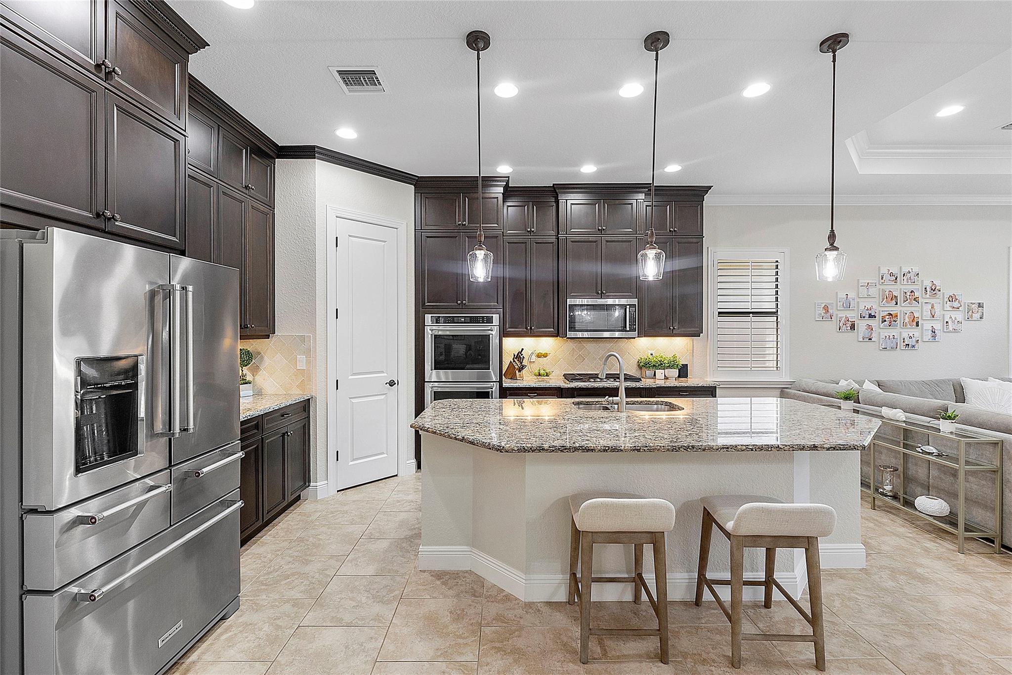Kitchen with center island, Cappuccino cabinets, stainless appliances, granite countertops & pendant lighting.