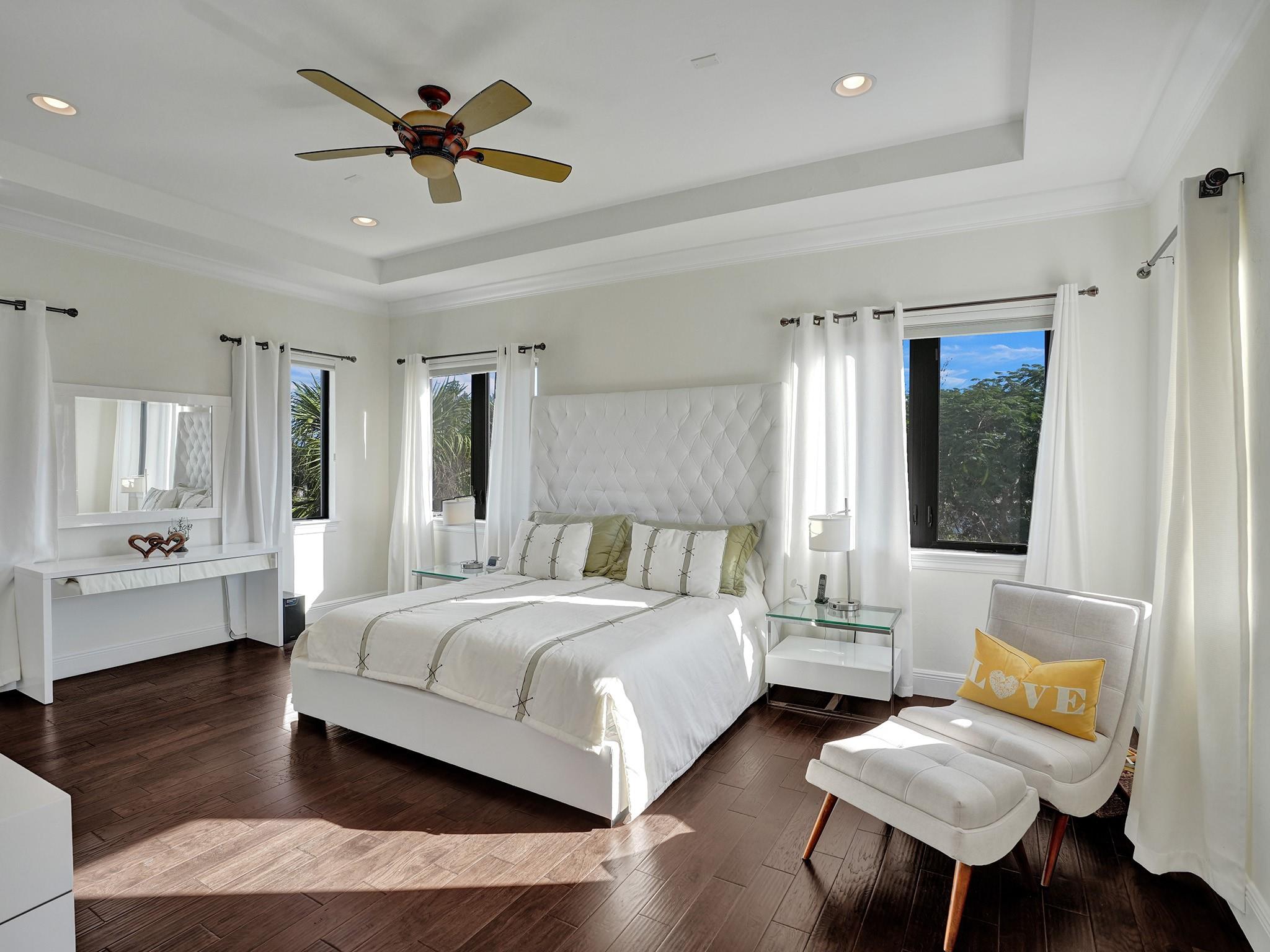 Warm wood floors and white furniture in the master bedroom highlight the lush green golf course through the windows.