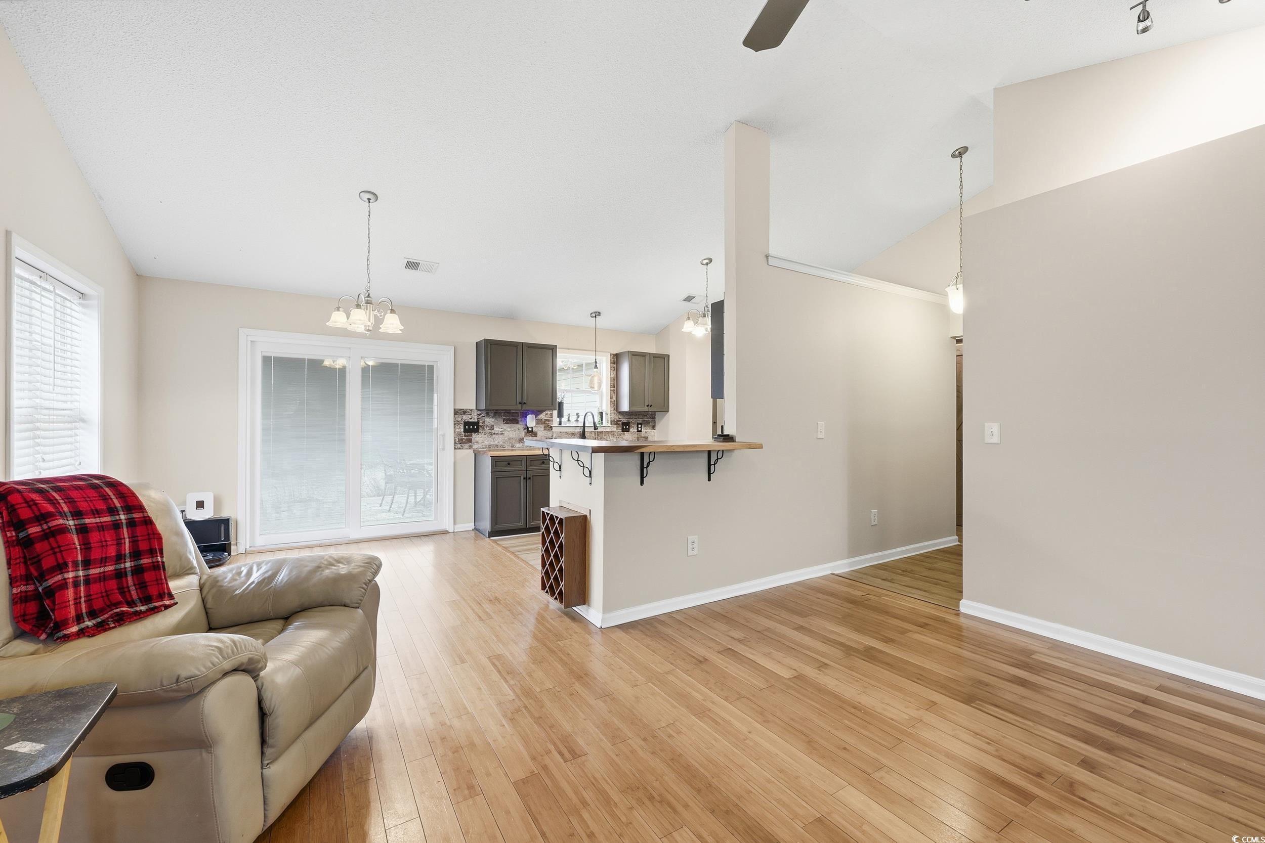 Living room with light wood-style flooring, vaulted ceiling, a chandelier, and ceiling fan