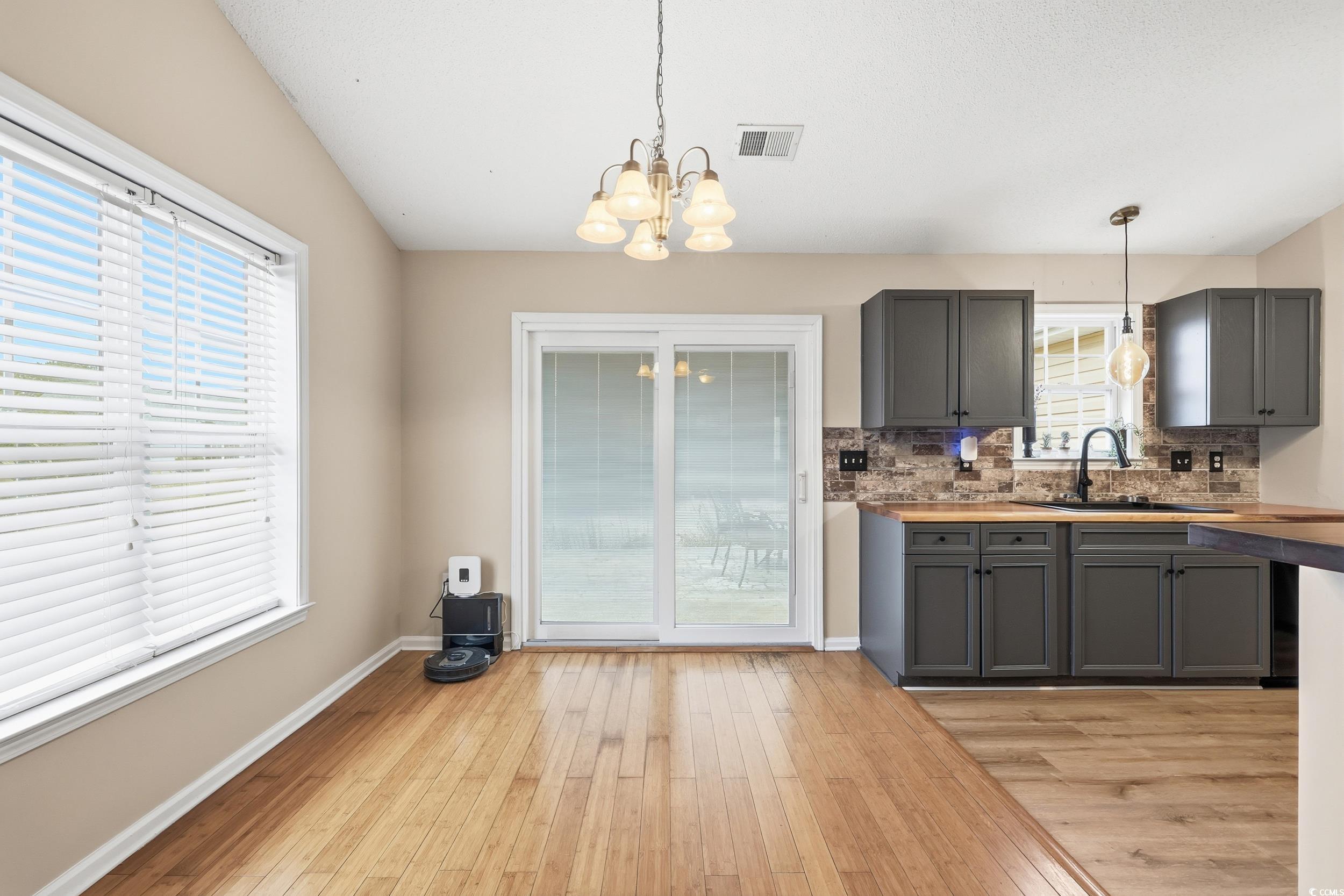 Kitchen featuring gray cabinetry, decorative backsplash, light wood-style floors, butcher block counters, and a chandelier