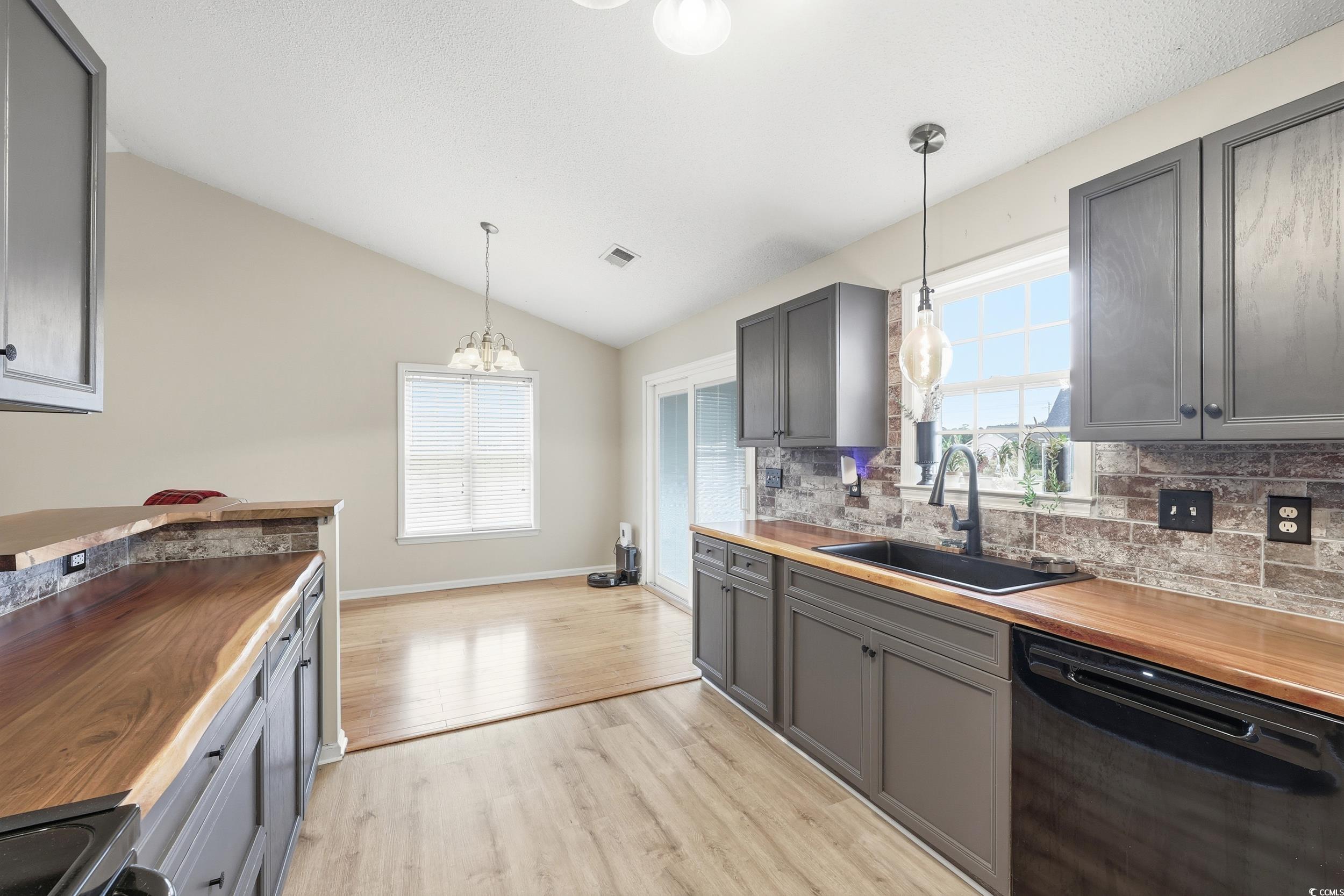 Kitchen featuring gray cabinets, lofted ceiling, black appliances, butcher block counters, and pendant lighting