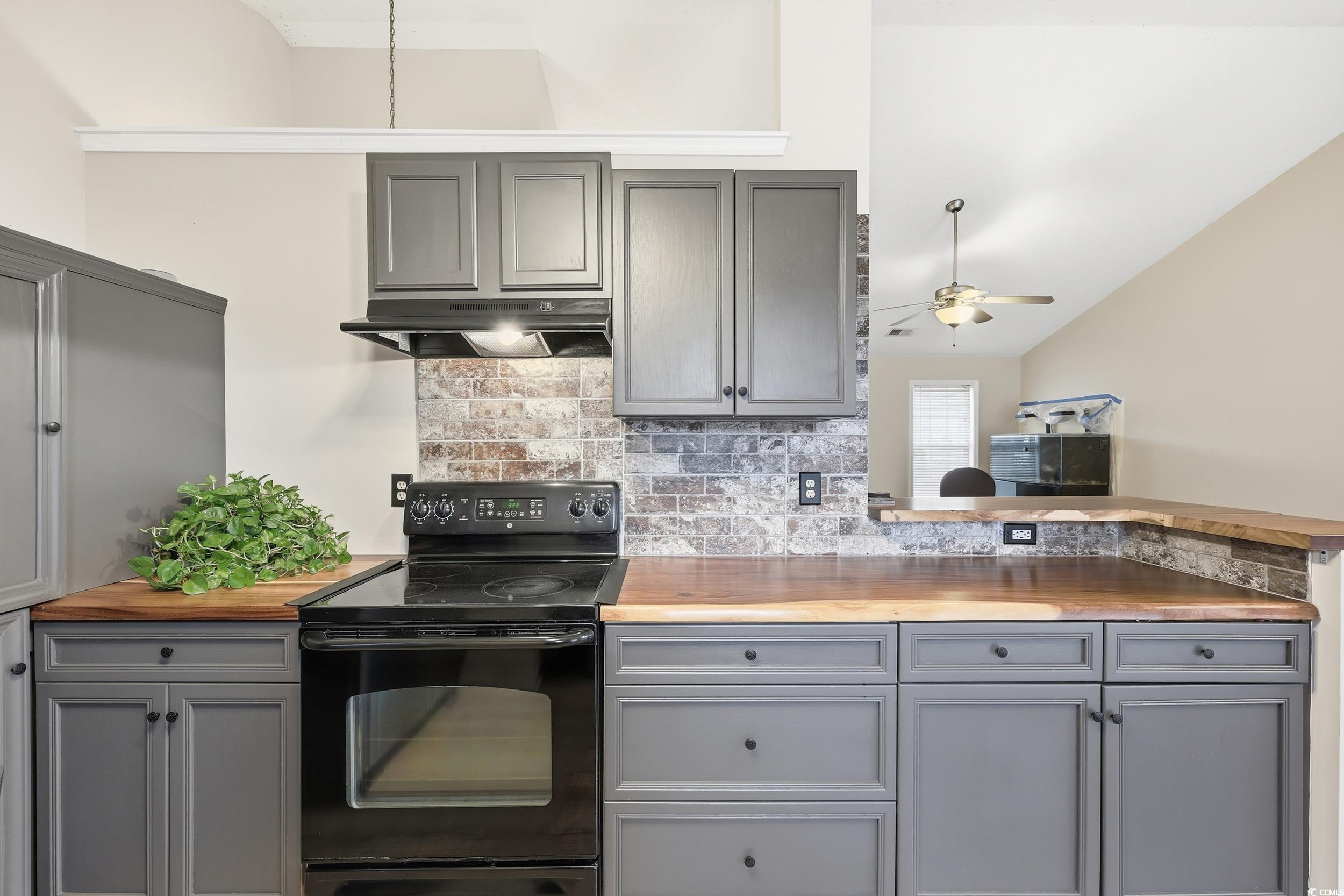 Kitchen with gray cabinets, black electric range oven, butcher block countertops, backsplash, and under cabinet range hood