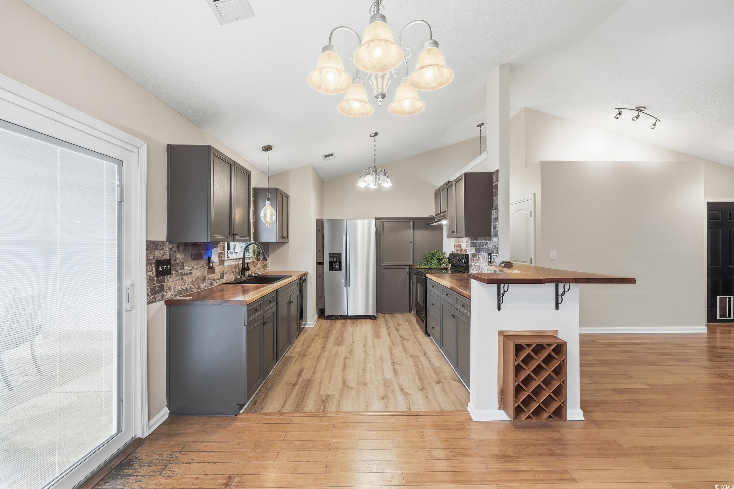 Kitchen with butcher block countertops, backsplash, vaulted ceiling, and stainless steel fridge