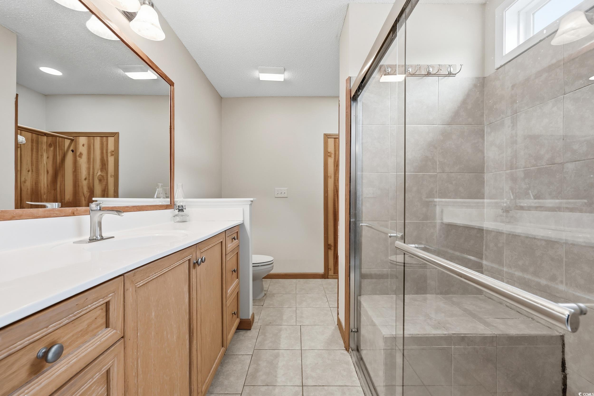 Bathroom with vanity, light tile patterned flooring, a stall shower, and a textured ceiling