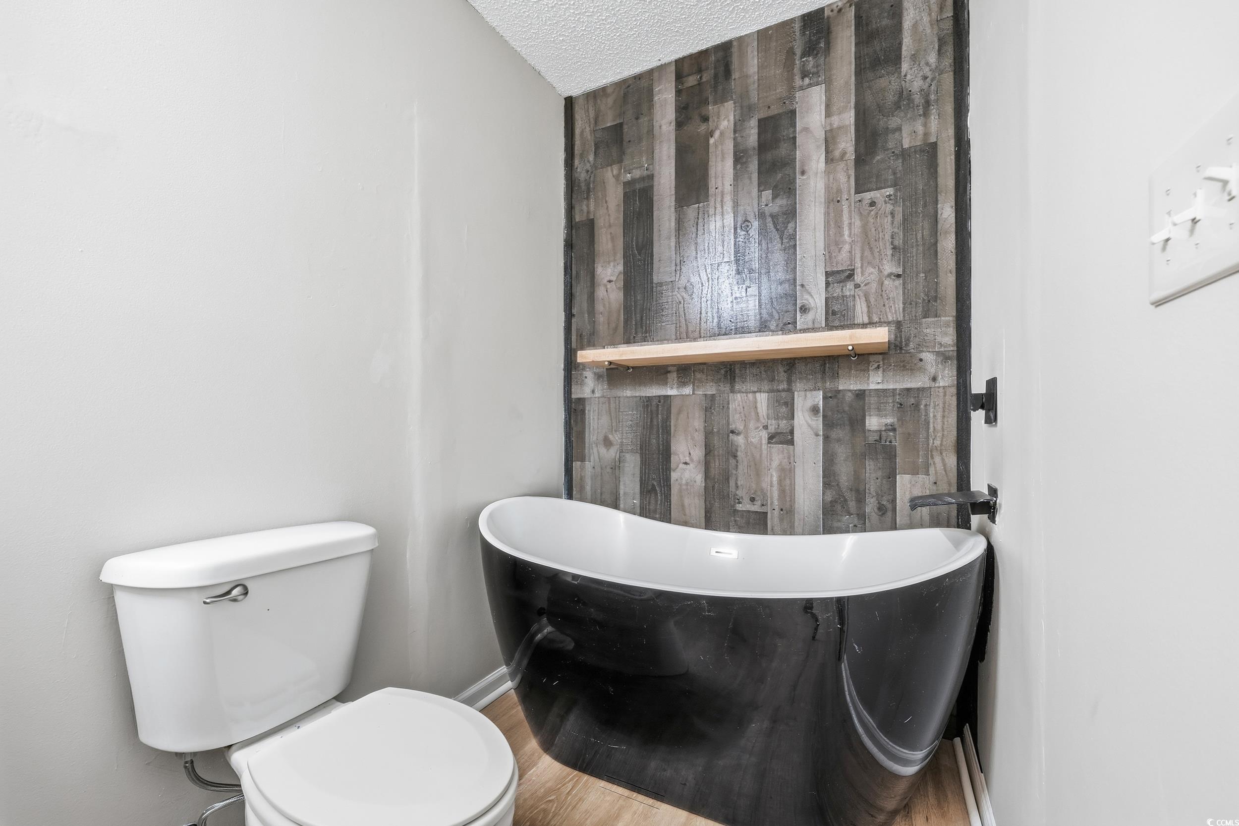 Full bathroom featuring a freestanding bath, a textured ceiling, wooden walls, and wood finished floors