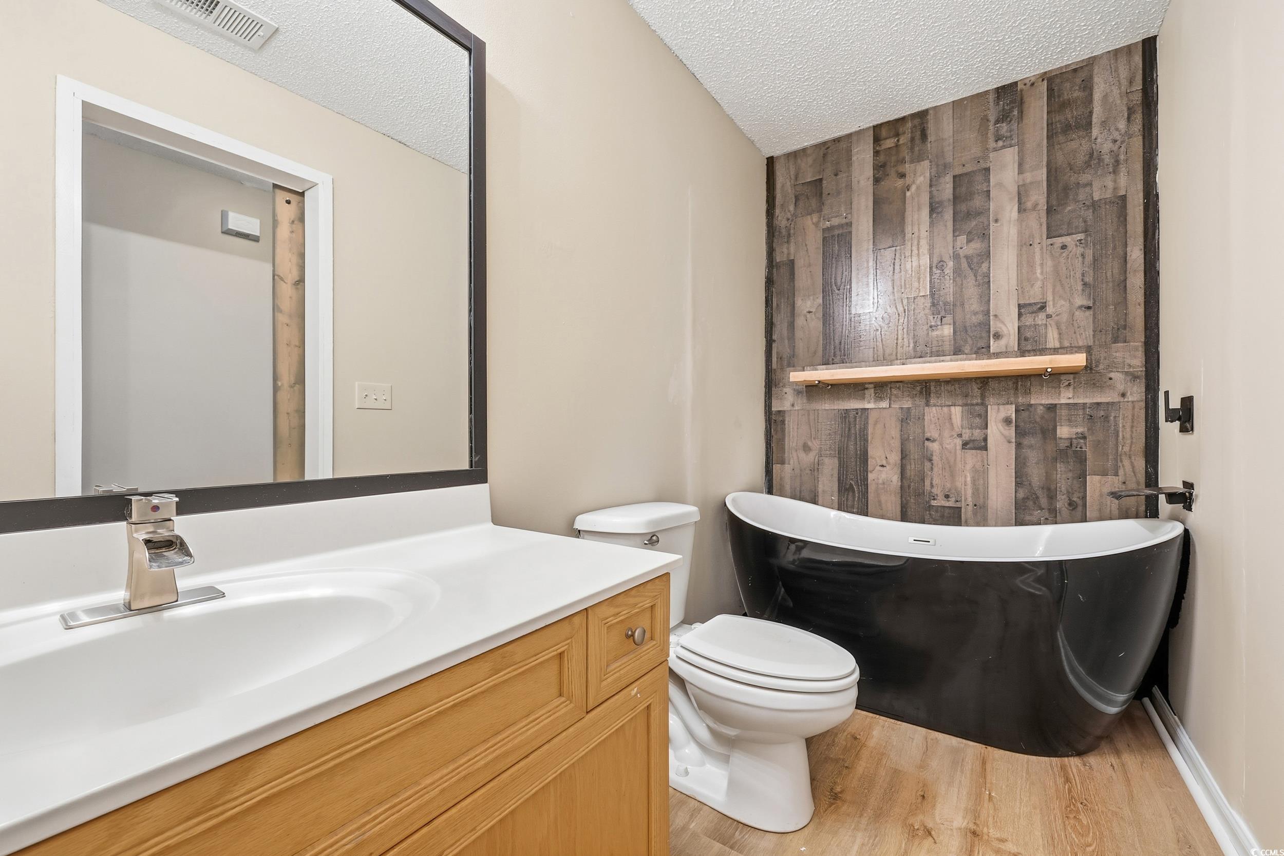 Bathroom featuring a freestanding tub, light wood-style floors, wood walls, a textured ceiling, and vanity