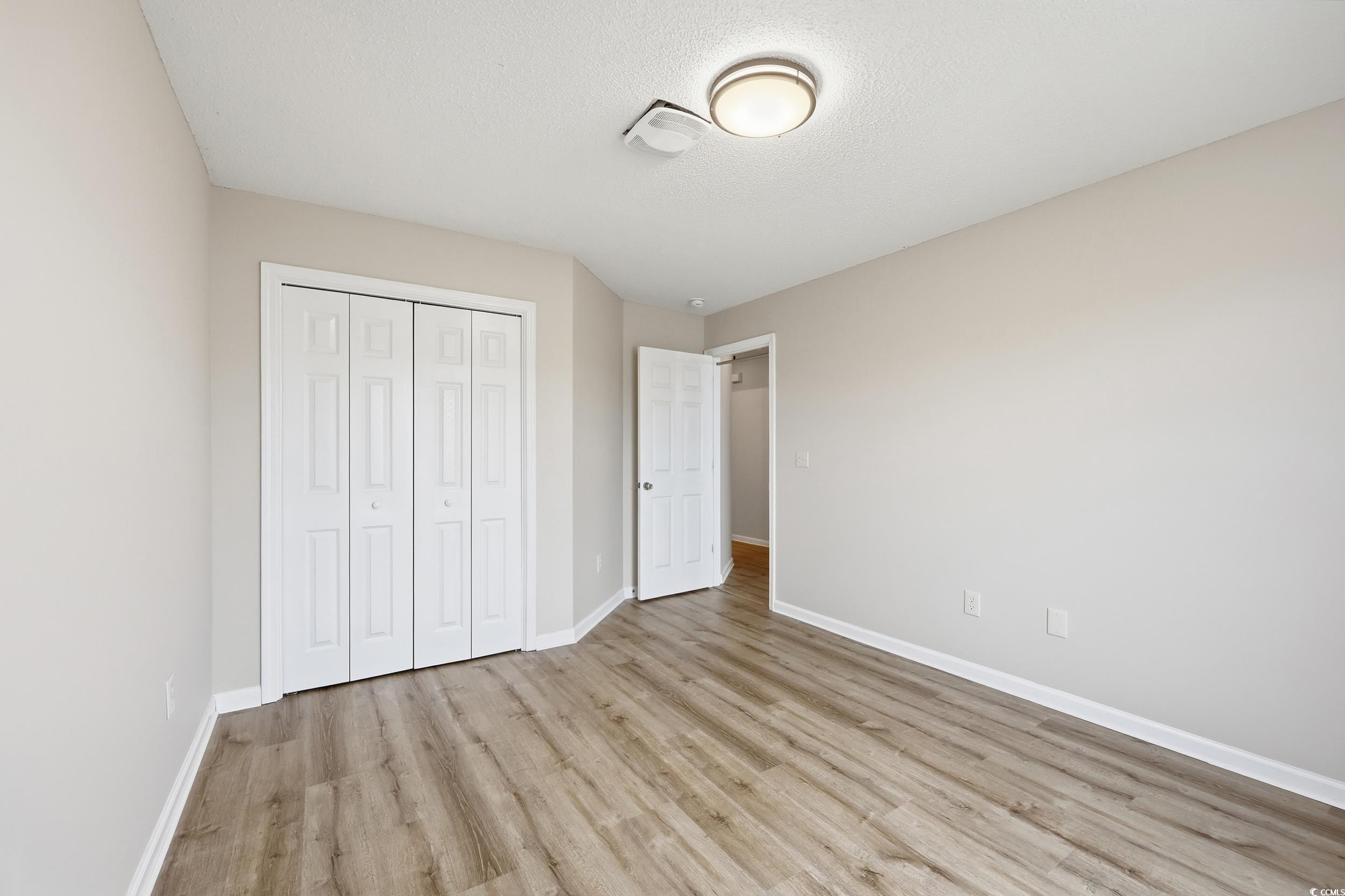 Unfurnished bedroom with light wood-style floors, a closet, and a textured ceiling