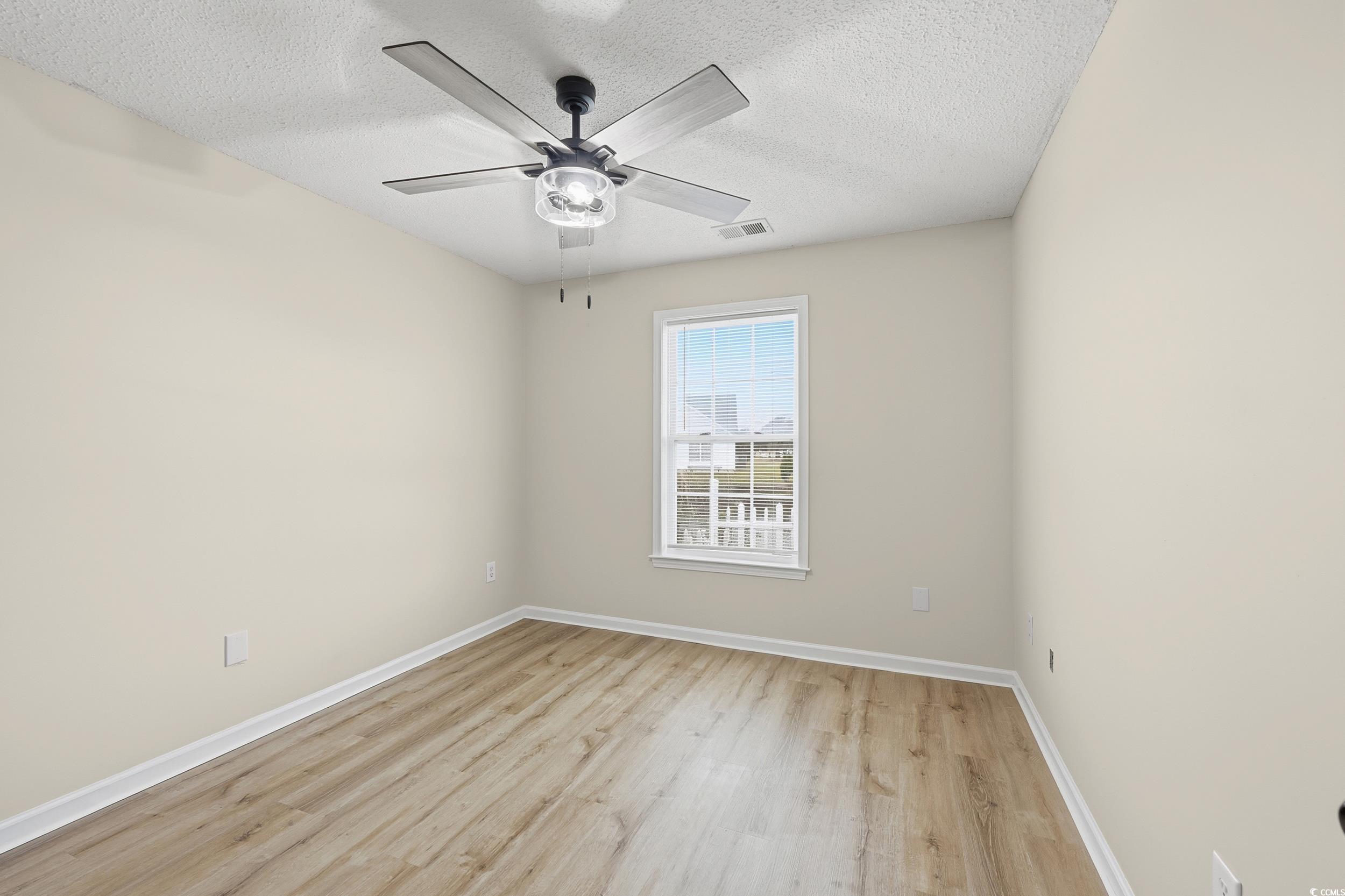 Empty room with light wood finished floors, a textured ceiling, and ceiling fan