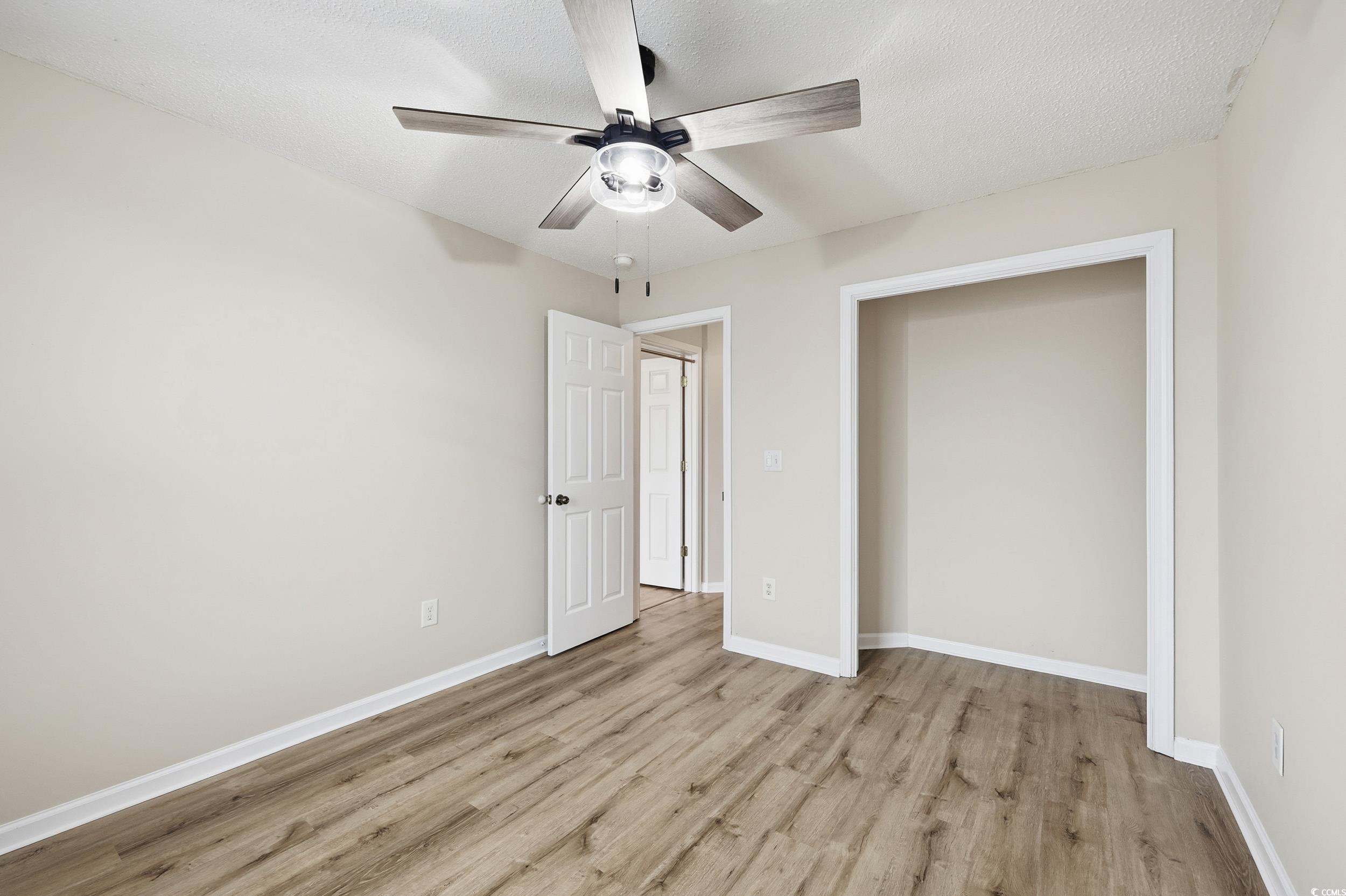 Unfurnished bedroom with light wood-type flooring, ceiling fan, and a textured ceiling