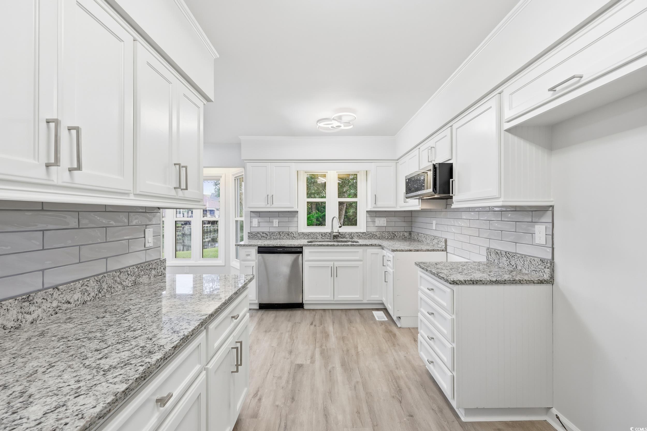 Kitchen with white cabinetry, decorative backsplash, light stone counters, stainless steel appliances, and crown molding