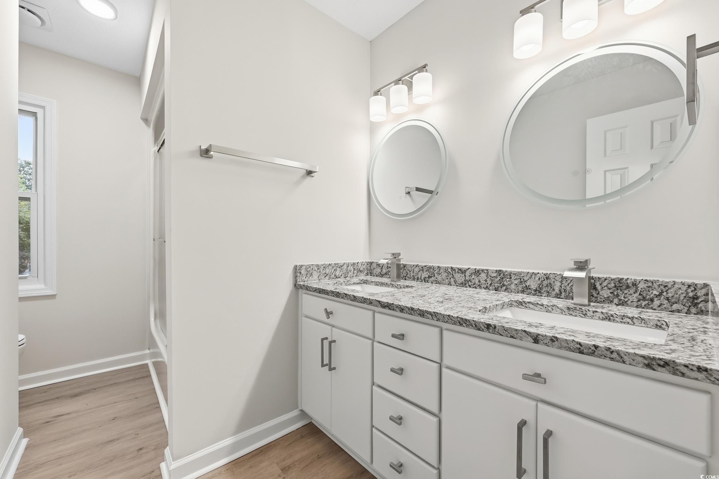 Full bathroom featuring double vanity, light wood-type flooring, and a stall shower