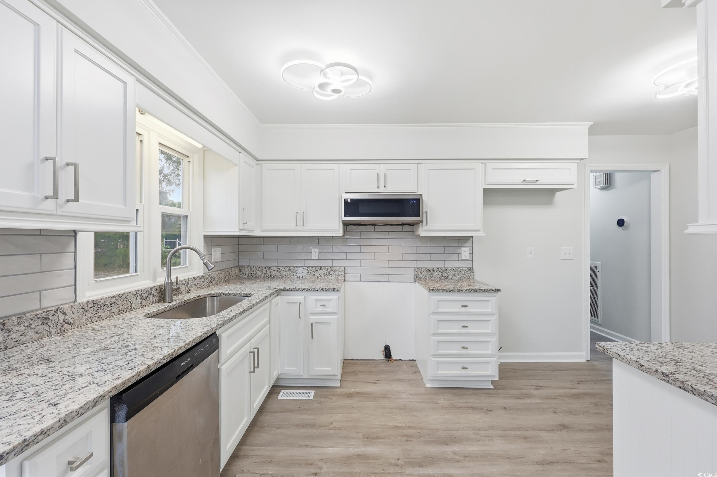 Kitchen featuring appliances with stainless steel finishes, backsplash, white cabinets, light stone countertops, and crown molding