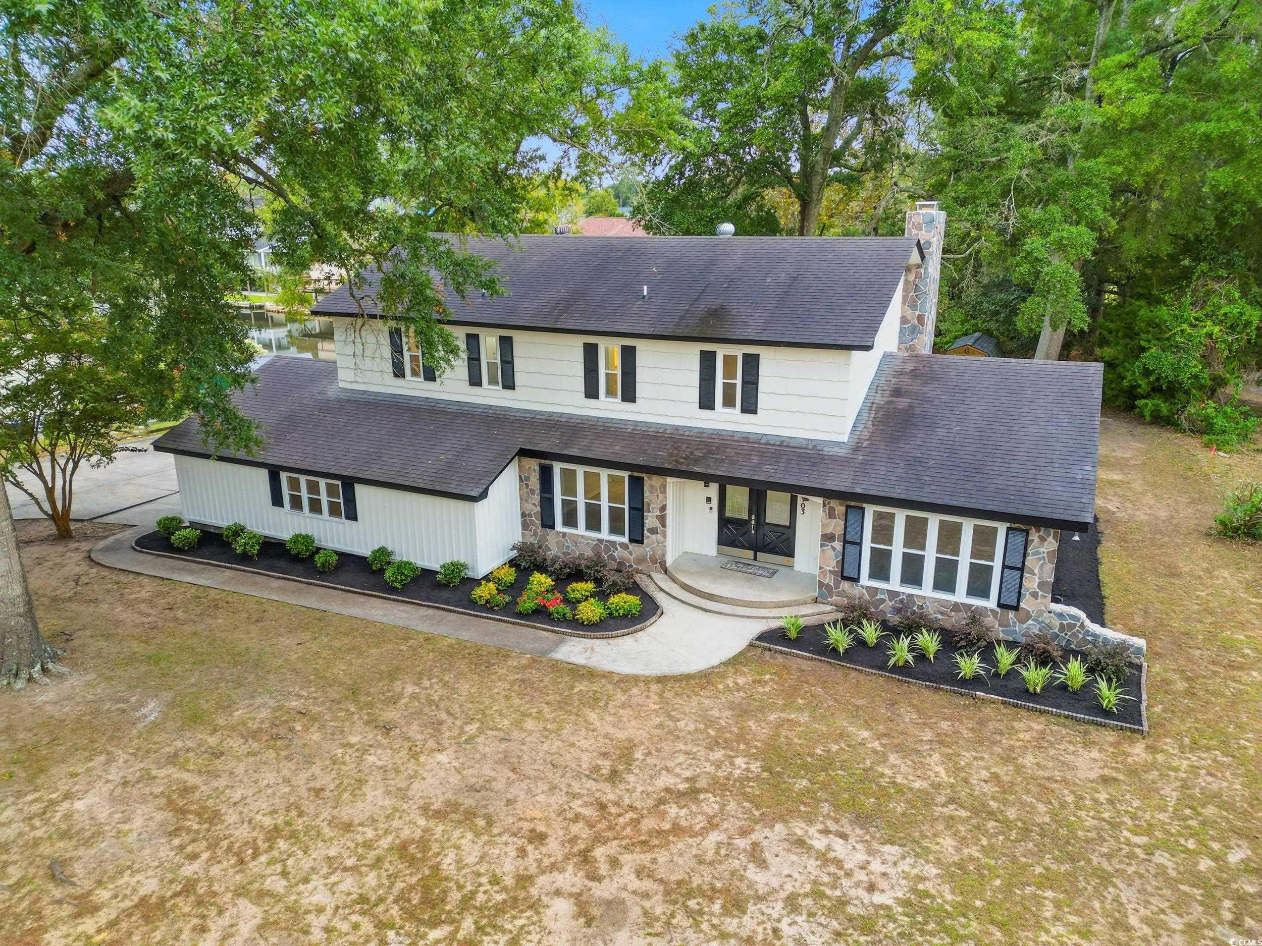 View of front of property with stone siding, a chimney, and roof with shingles