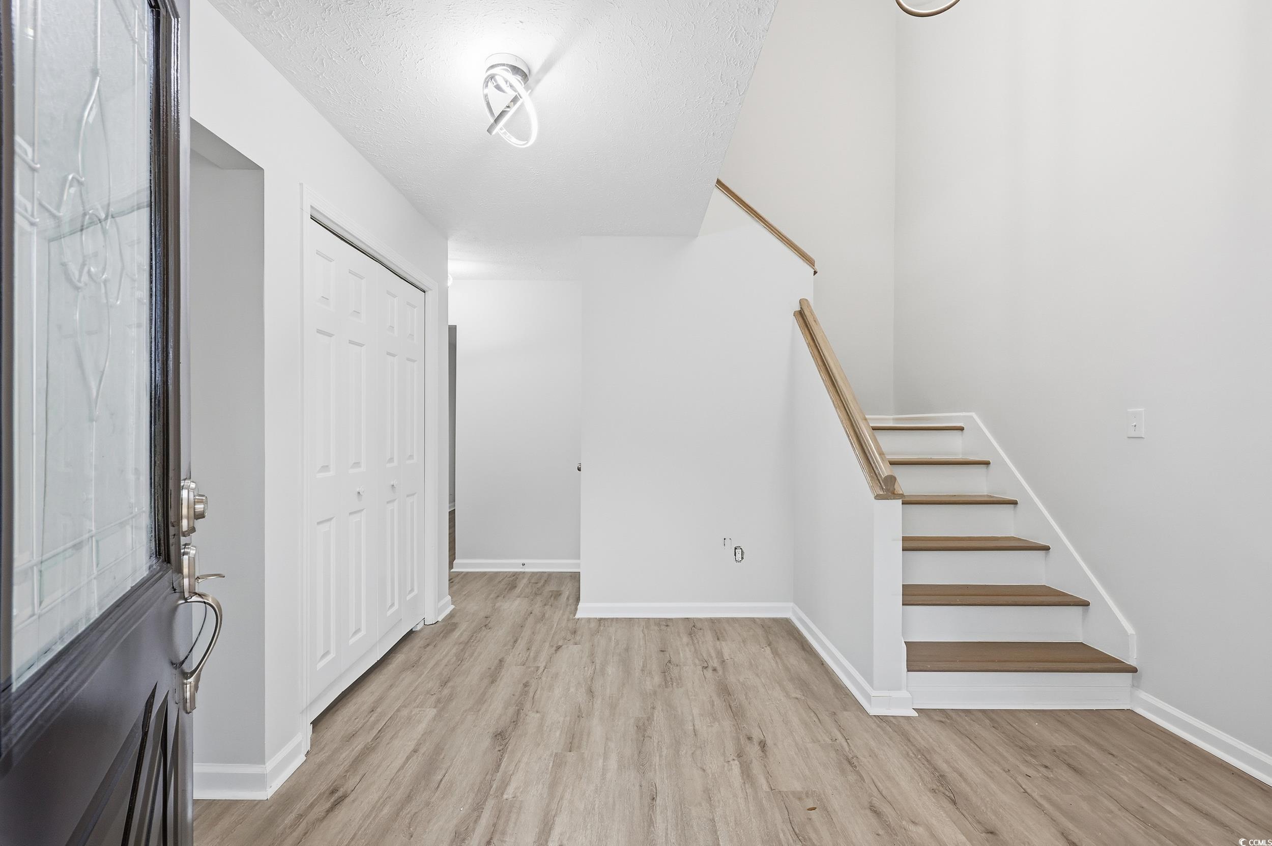 Foyer entrance featuring light wood-style flooring, stairs, and a textured ceiling