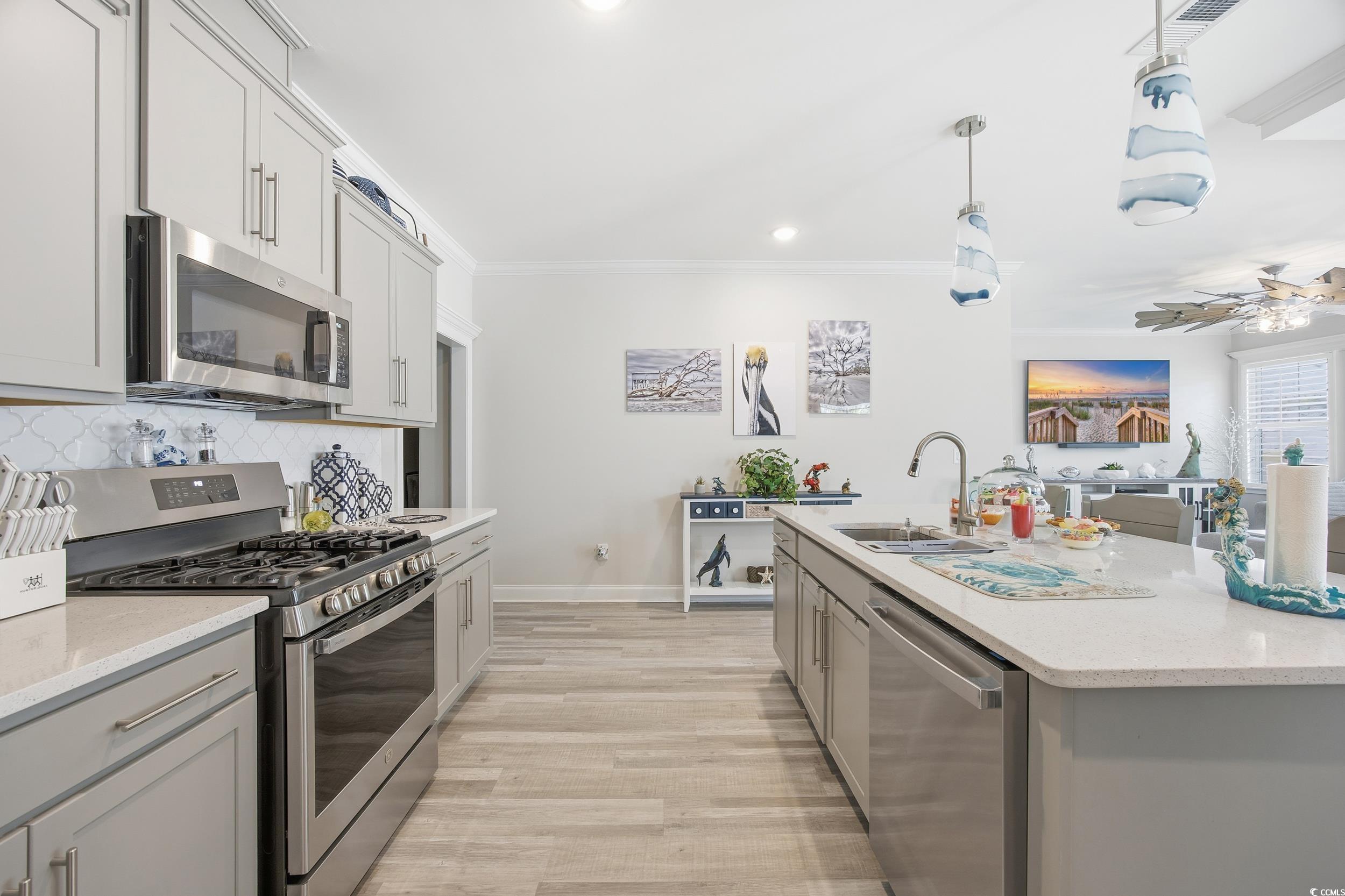 Kitchen featuring stainless steel appliances, gray cabinetry, light stone counters, hanging light fixtures, and light wood finished floors