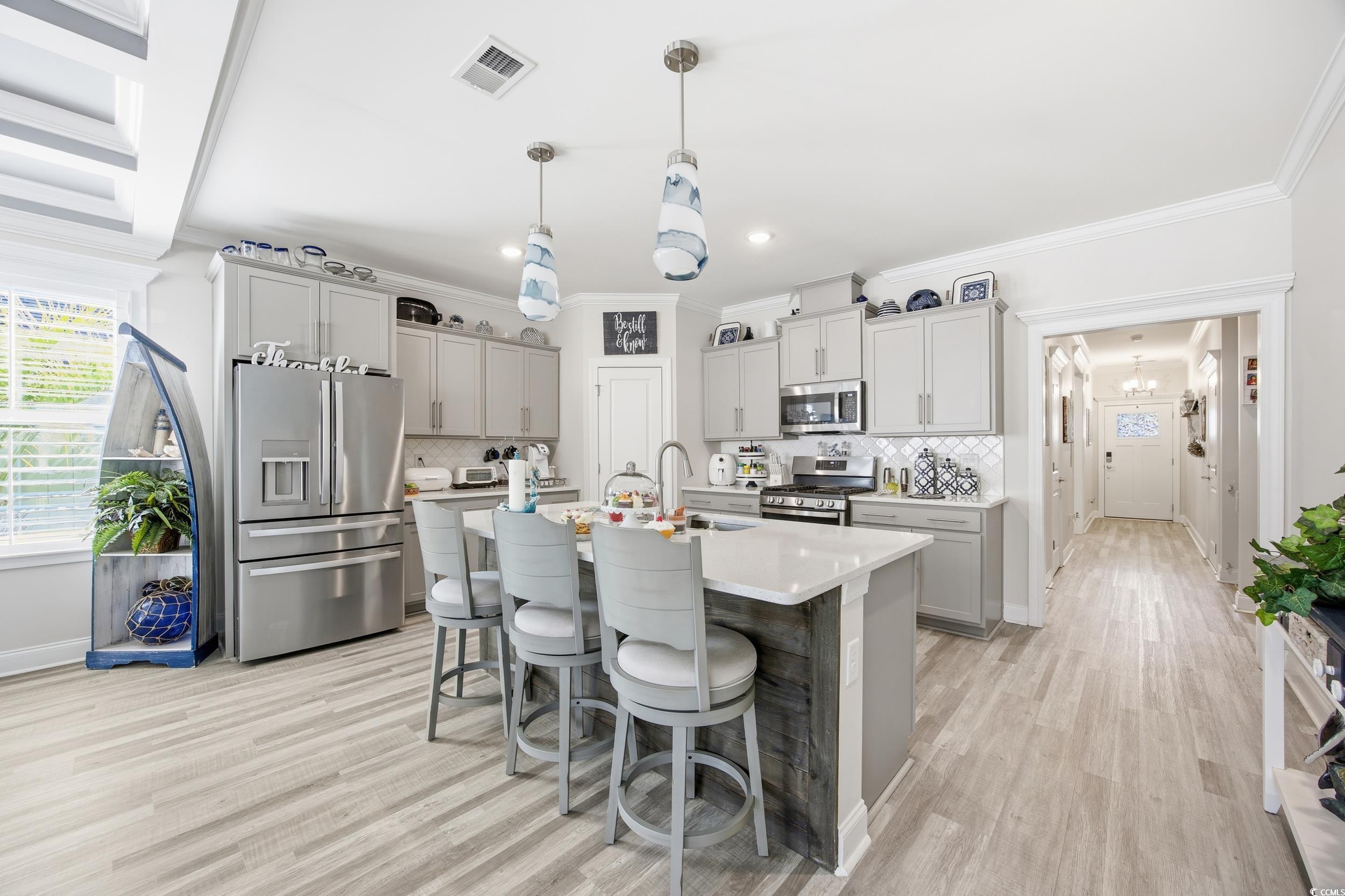 Kitchen with gray cabinets, a kitchen bar, appliances with stainless steel finishes, ornamental molding, and decorative light fixtures