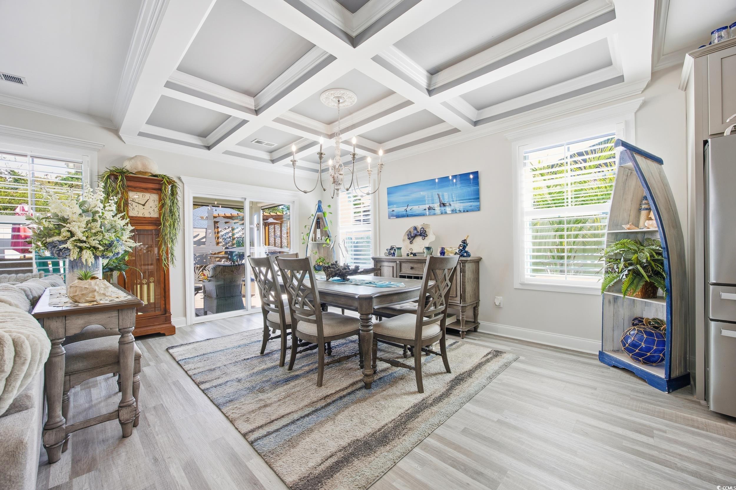 Dining area featuring light wood-style floors, plenty of natural light, beamed ceiling, coffered ceiling, and crown molding