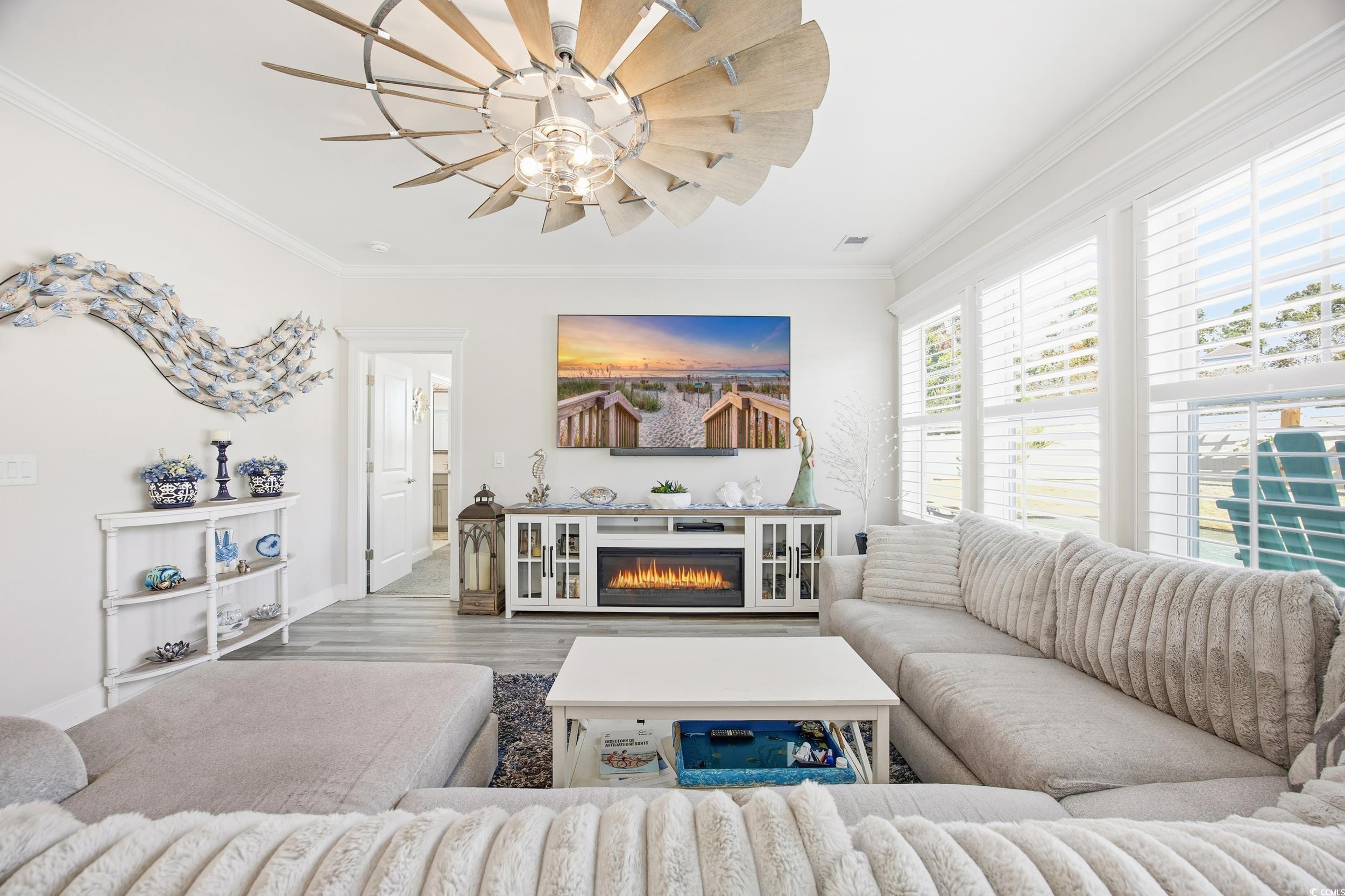 Living area featuring crown molding, wood finished floors, a glass covered fireplace, and a ceiling fan