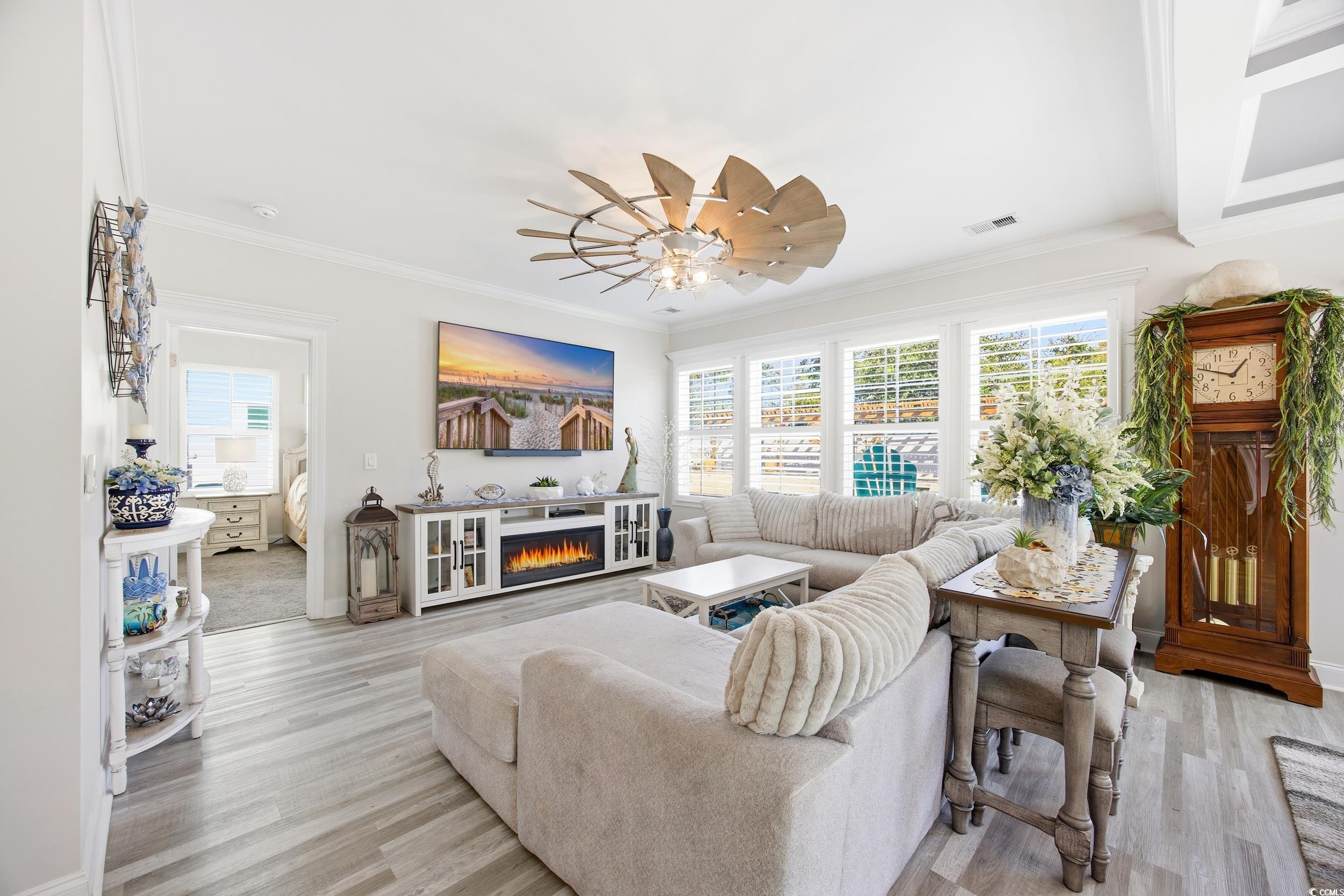 Living area with crown molding, a lit fireplace, light wood-style floors, and a ceiling fan