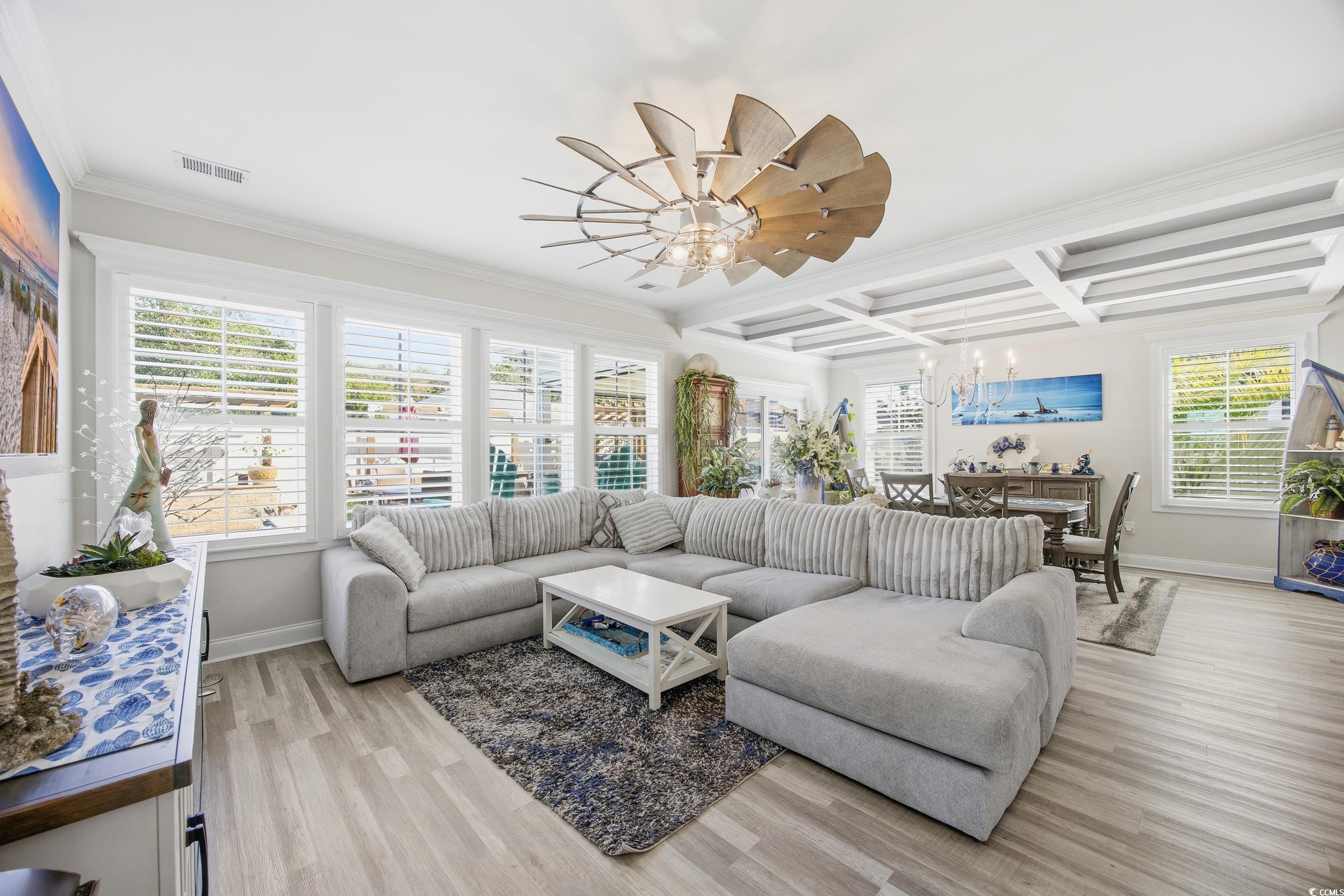 Living room with coffered ceiling, light wood-type flooring, crown molding, beamed ceiling, and a ceiling fan