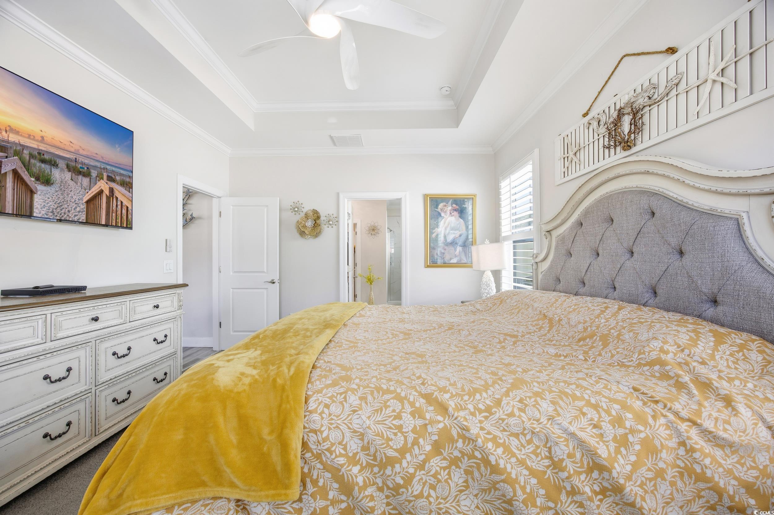 Bedroom with connected bathroom, ornamental molding, ceiling fan, and a tray ceiling