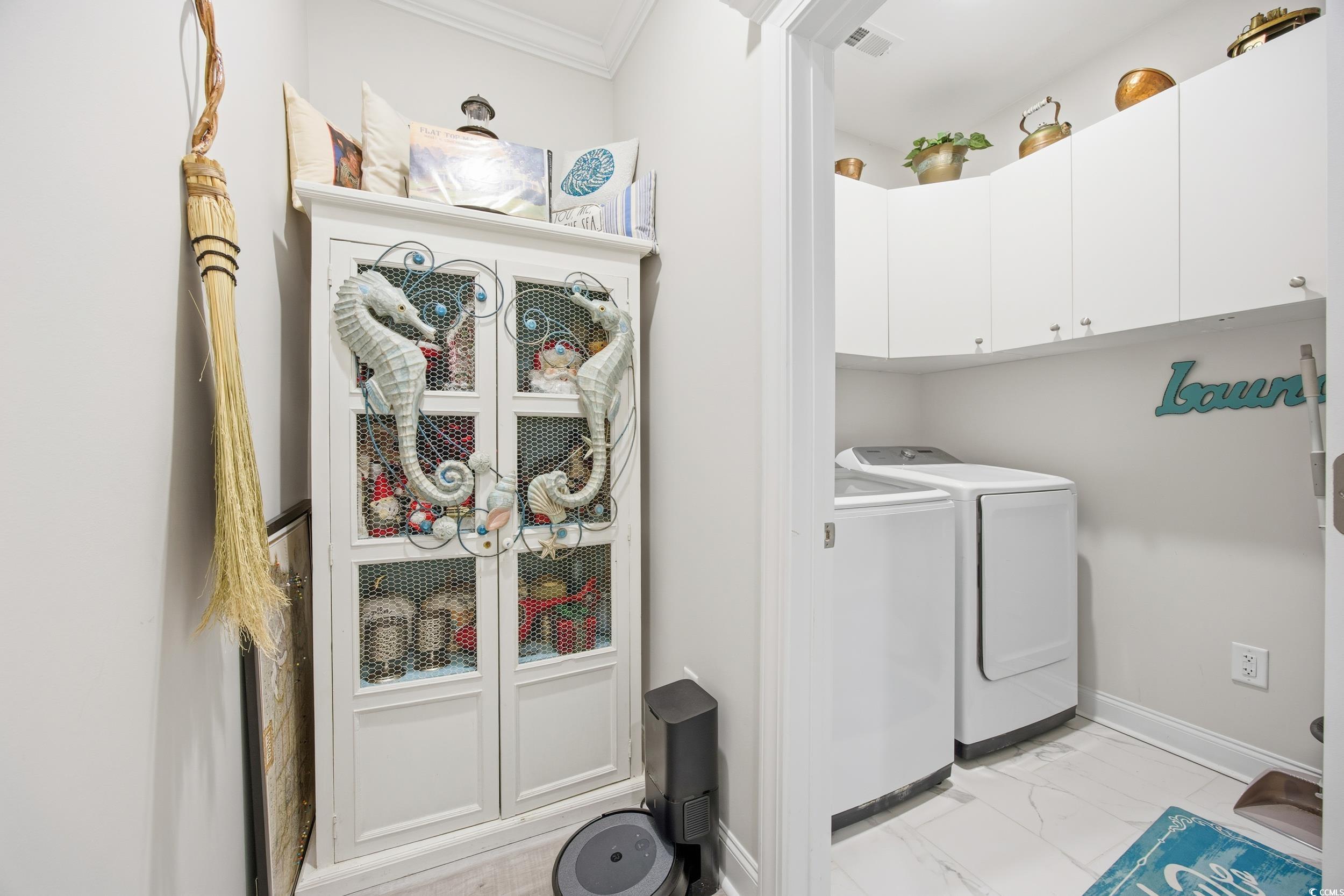 Laundry room with light marble finish flooring, washer and dryer, ornamental molding, and cabinet space