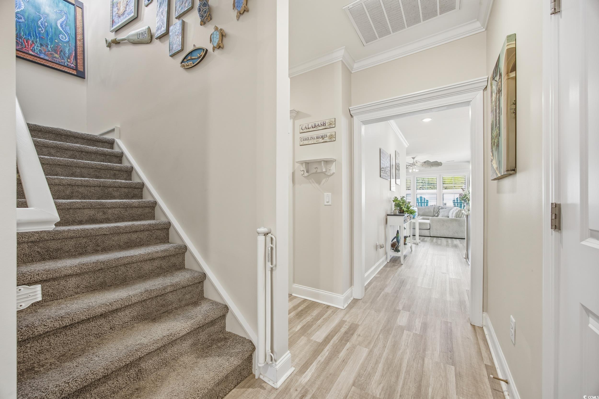 Staircase with wood finished floors, ornamental molding, and ceiling fan