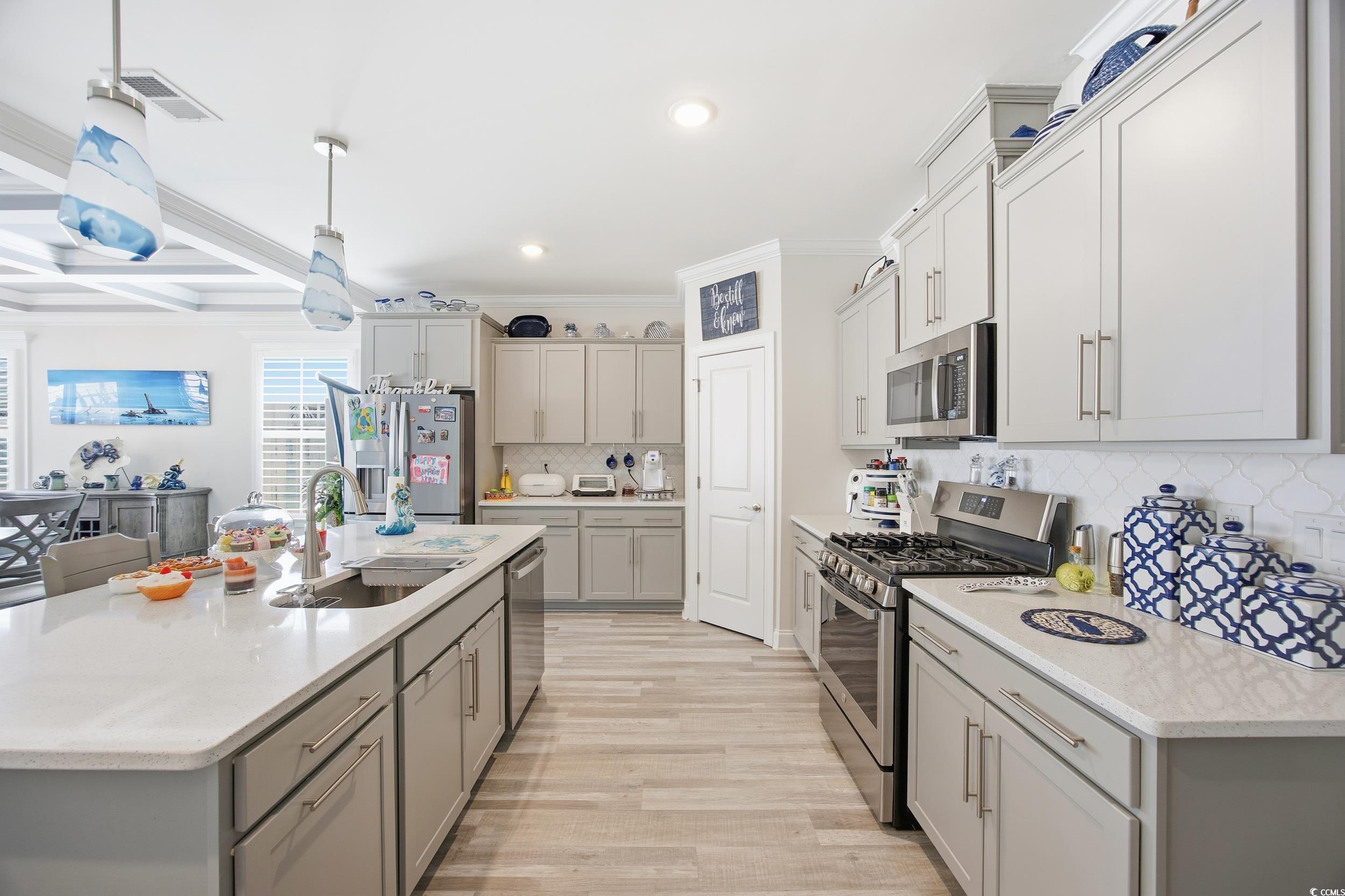 Kitchen featuring stainless steel appliances, gray cabinetry, hanging light fixtures, beam ceiling, and a kitchen island with sink