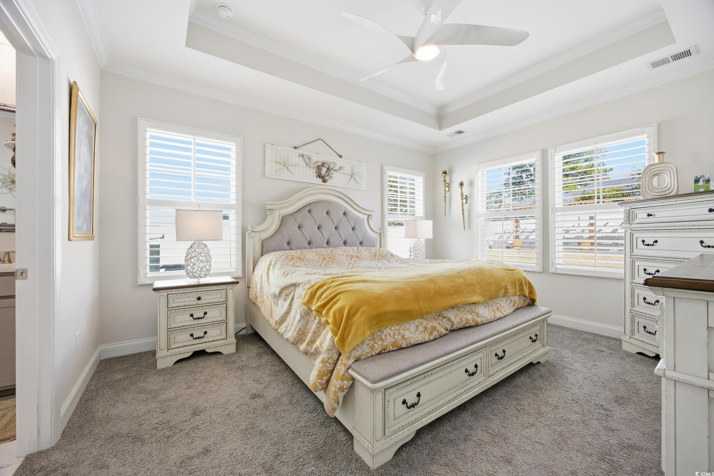 Bedroom with a tray ceiling, crown molding, light colored carpet, and a ceiling fan