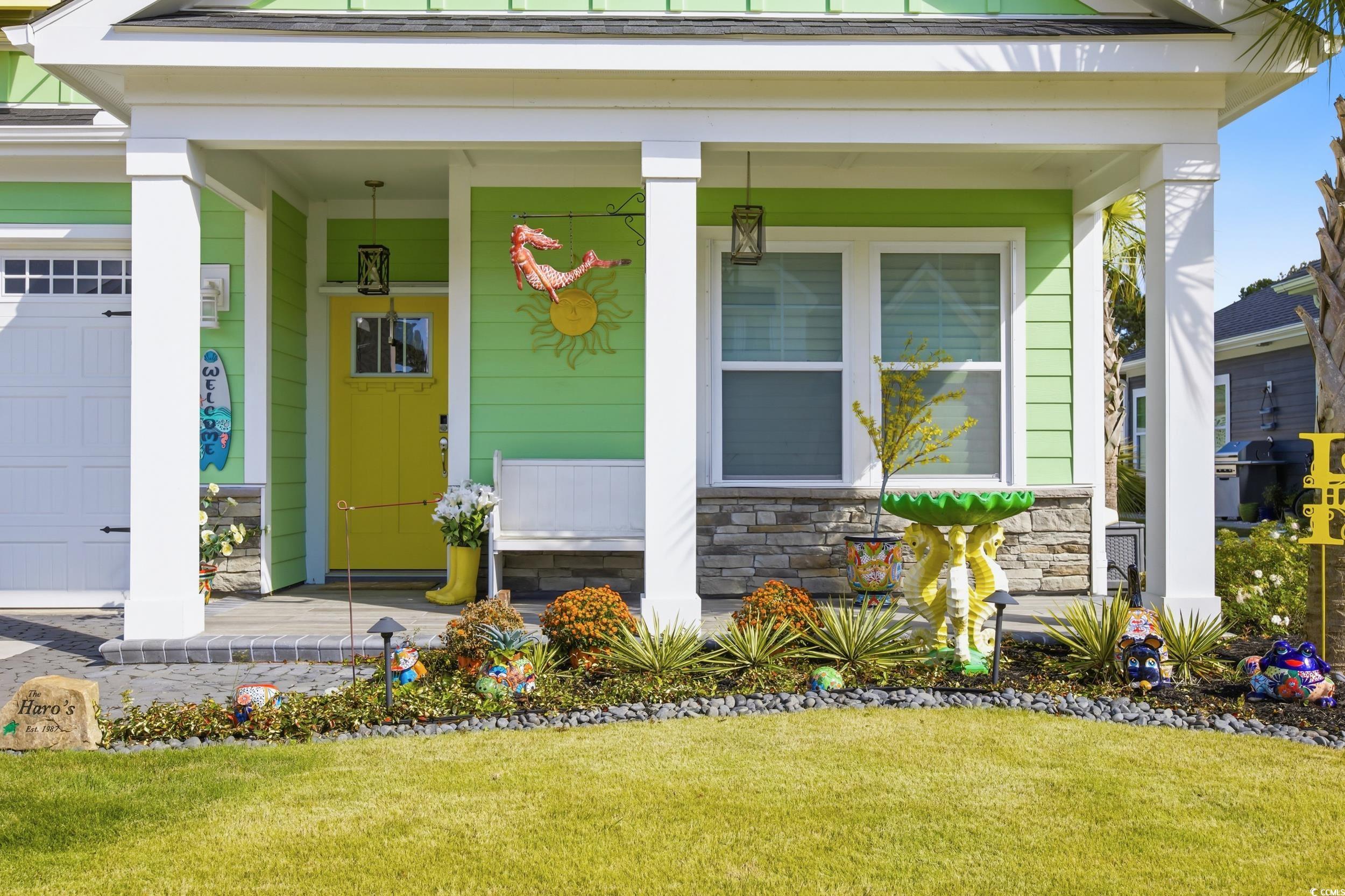 View of exterior entry with a porch, stone siding, a yard, and an attached garage