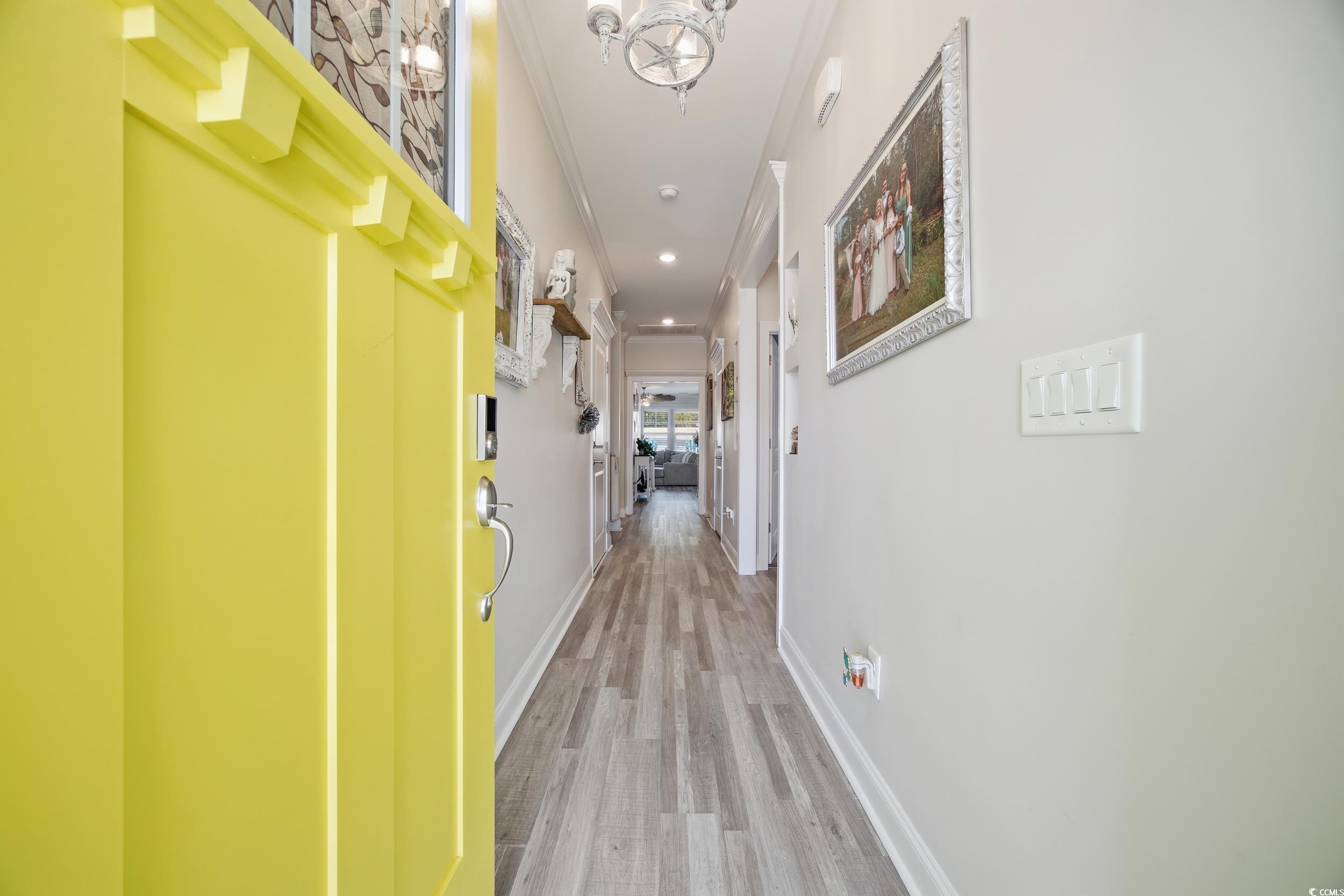 Hallway featuring light wood-style flooring, ornamental molding, and a chandelier