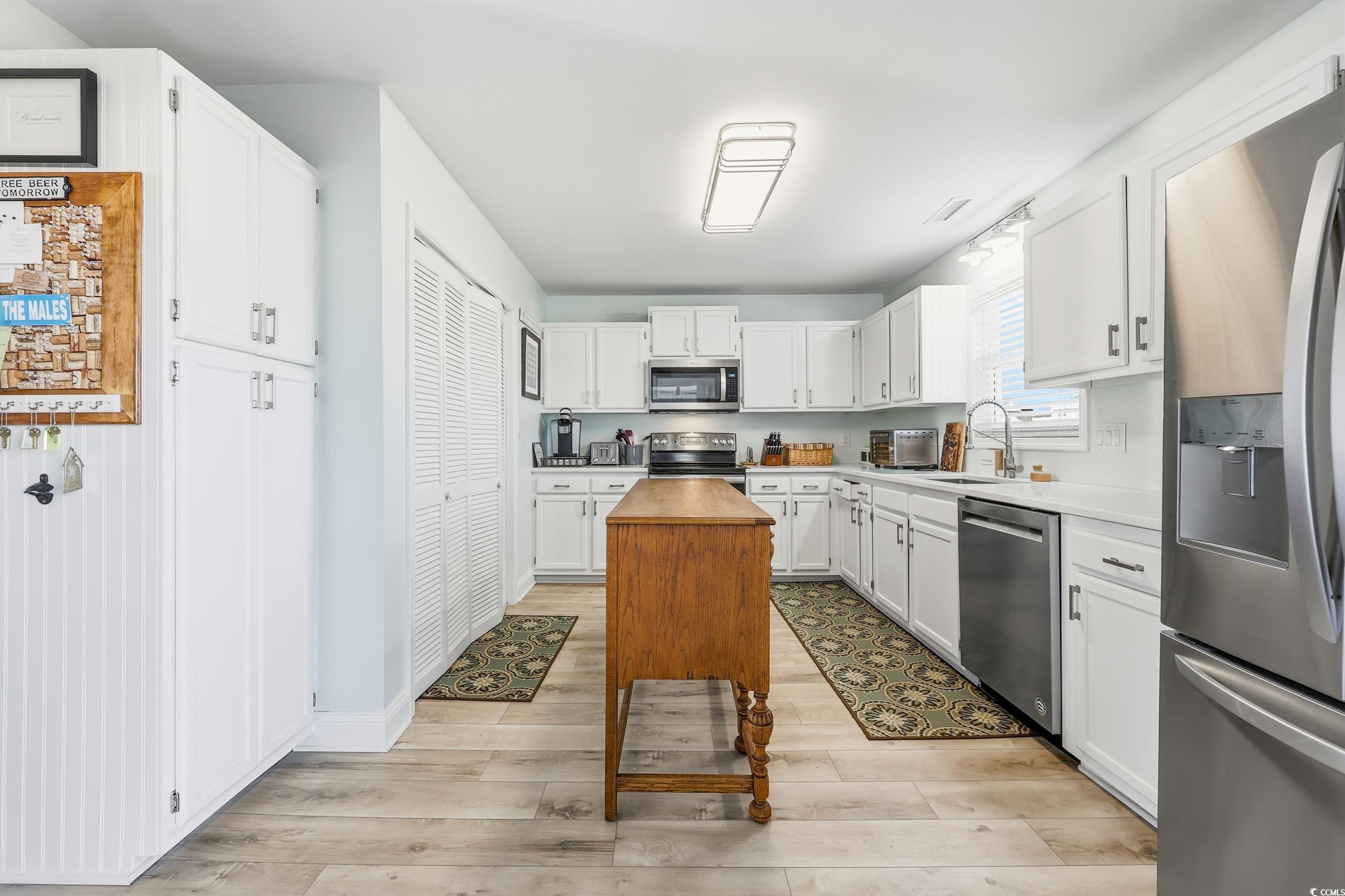 Kitchen featuring stainless steel appliances, white cabinets, light wood-style floors, and wooden counters