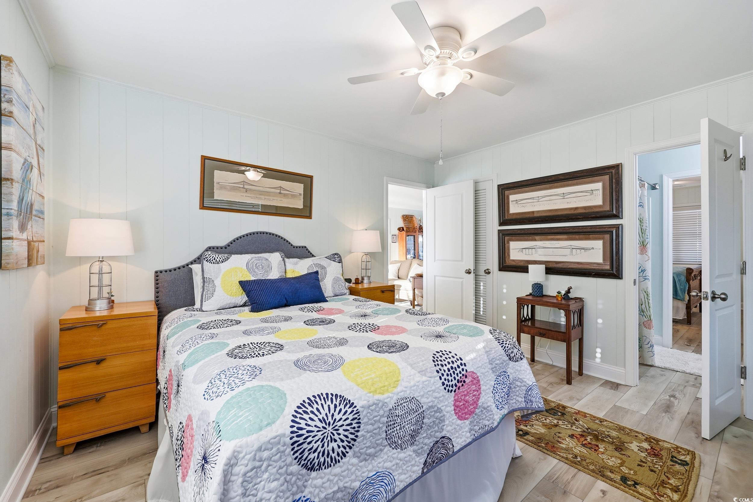 Bedroom featuring light wood finished floors, a ceiling fan, wooden walls, and a closet