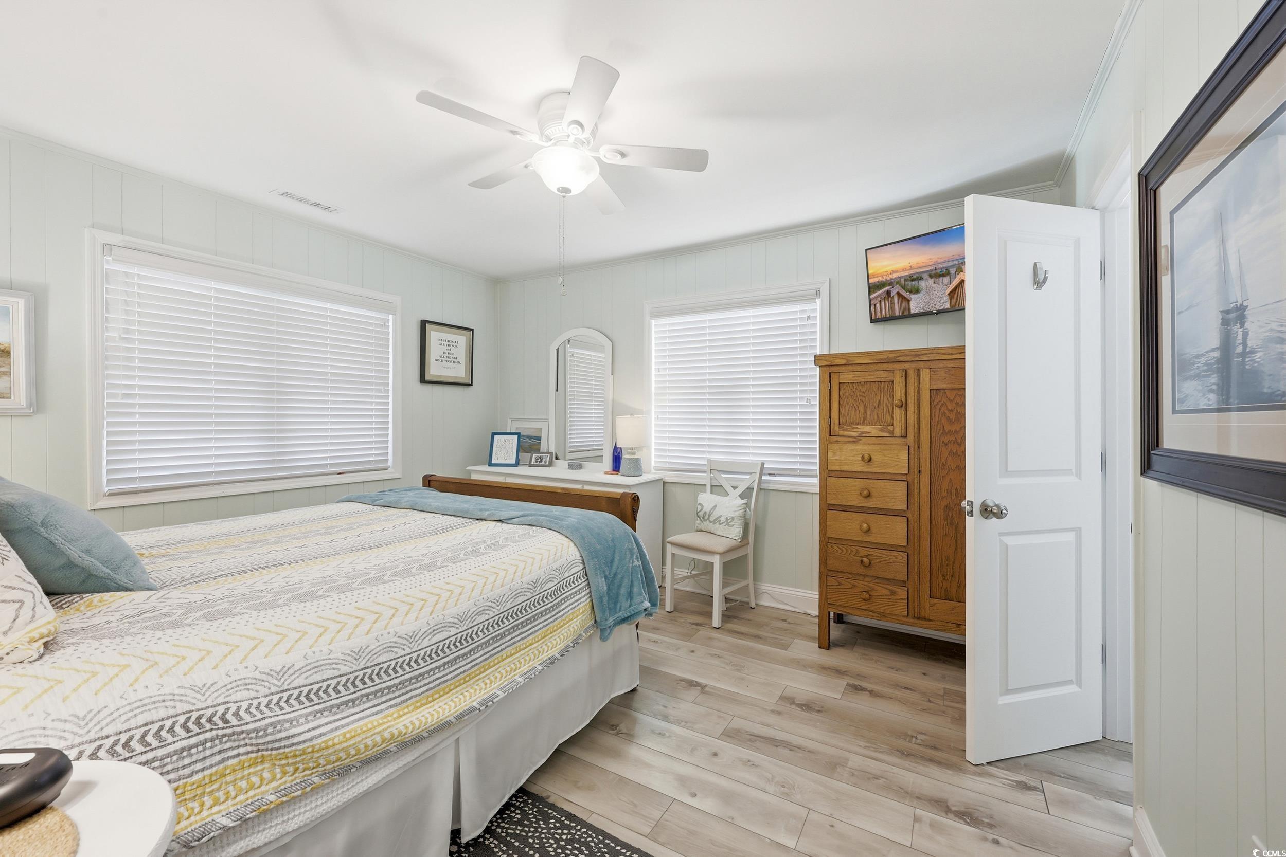 Bedroom with light wood-style floors, wooden walls, and ceiling fan