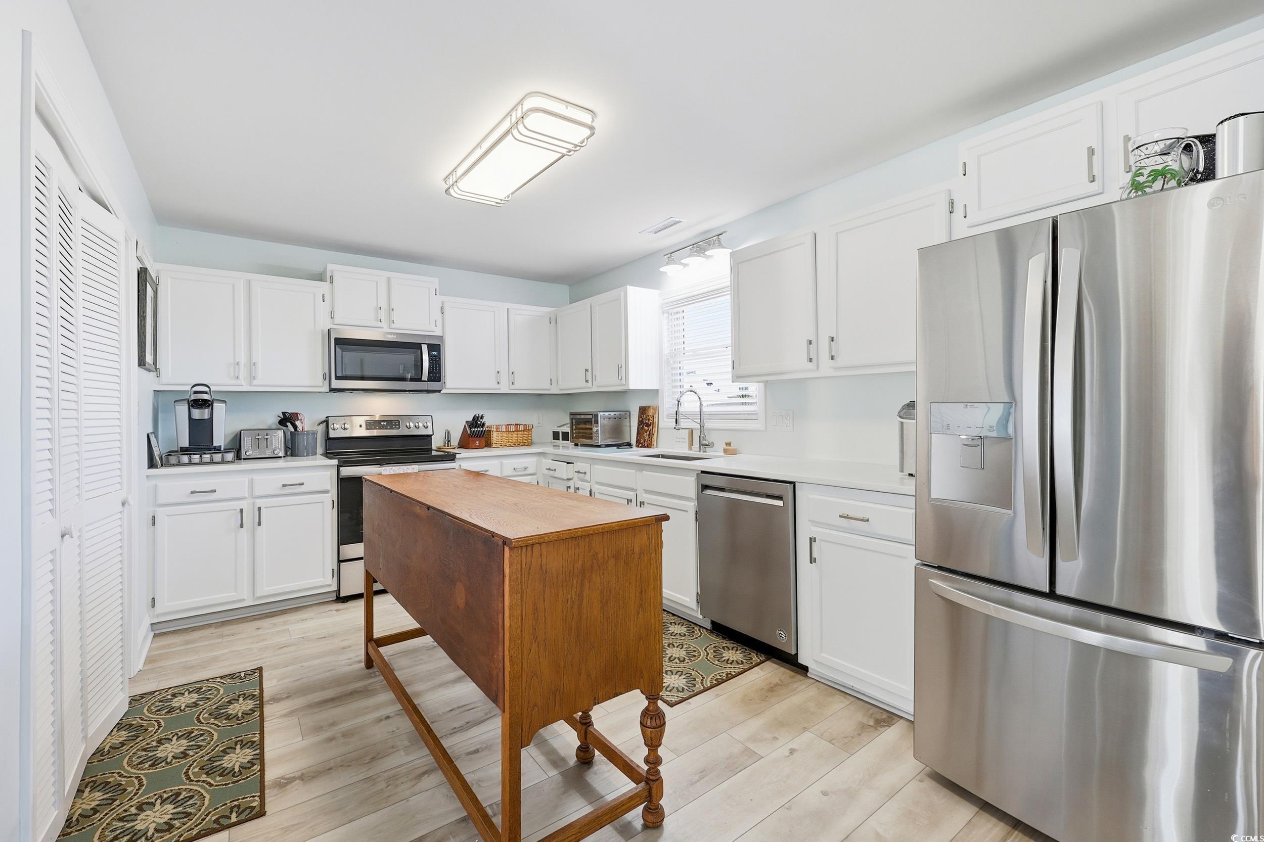 Kitchen with appliances with stainless steel finishes, white cabinetry, light countertops, and light wood-style floors