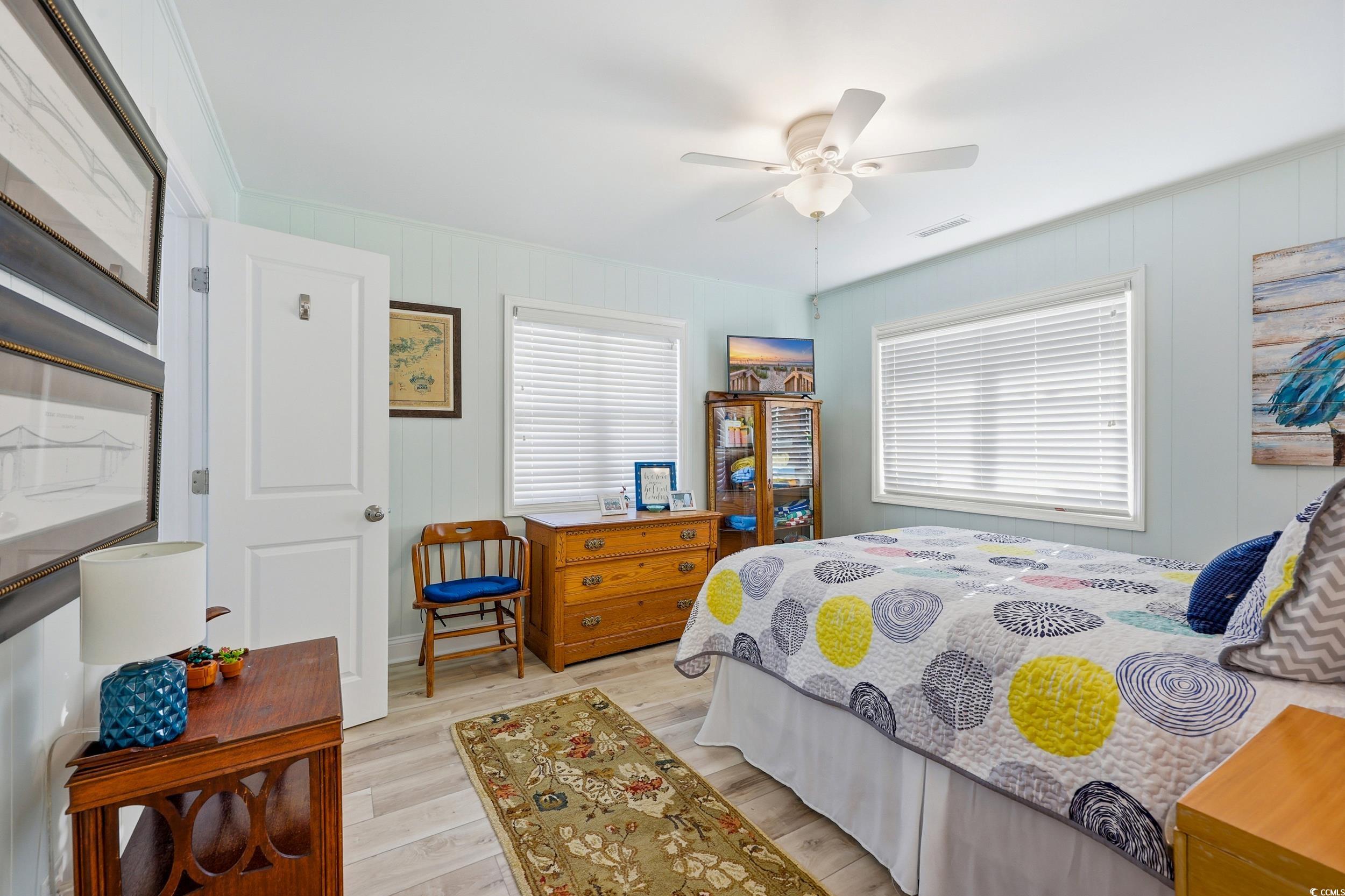 Bedroom with light wood-type flooring, multiple windows, a ceiling fan, and wood walls