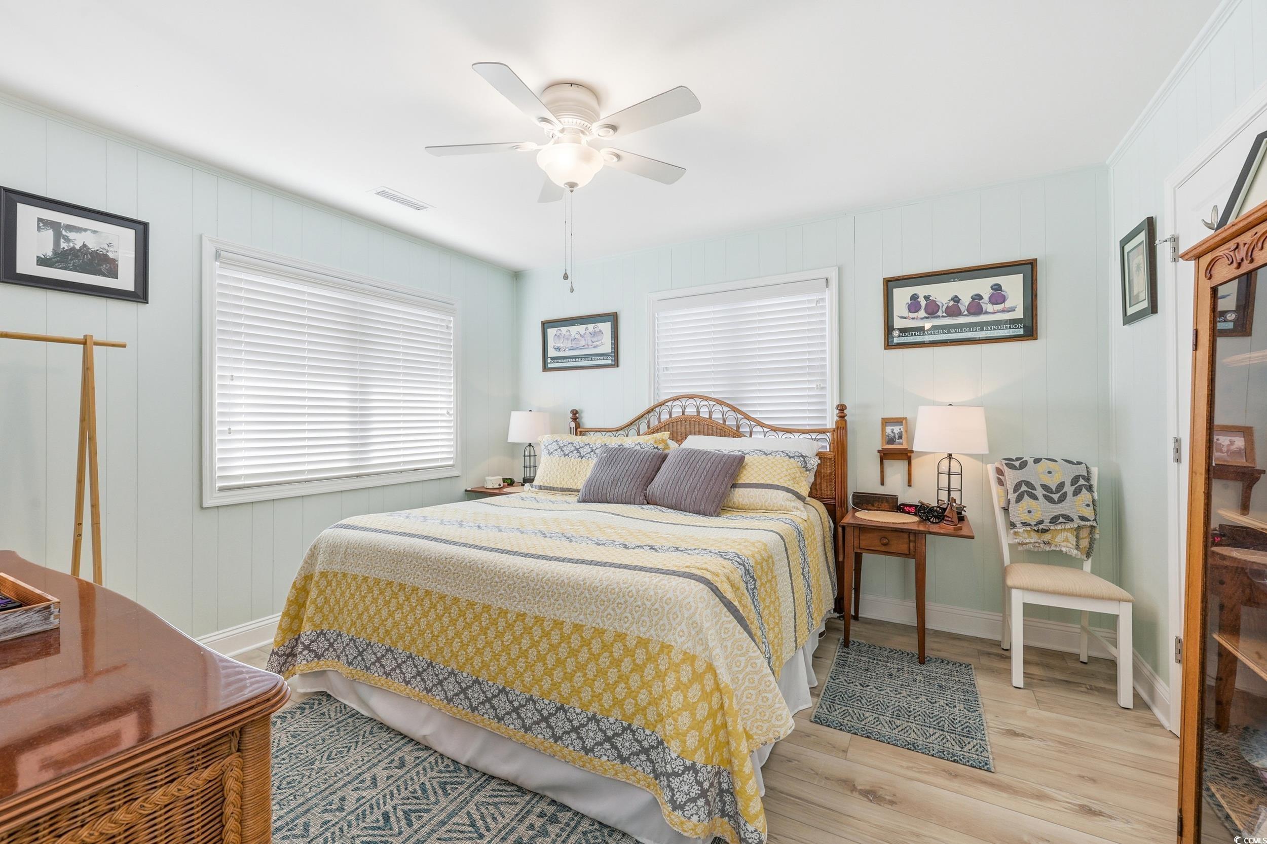 Bedroom featuring light wood-type flooring, multiple windows, ceiling fan, and wooden walls