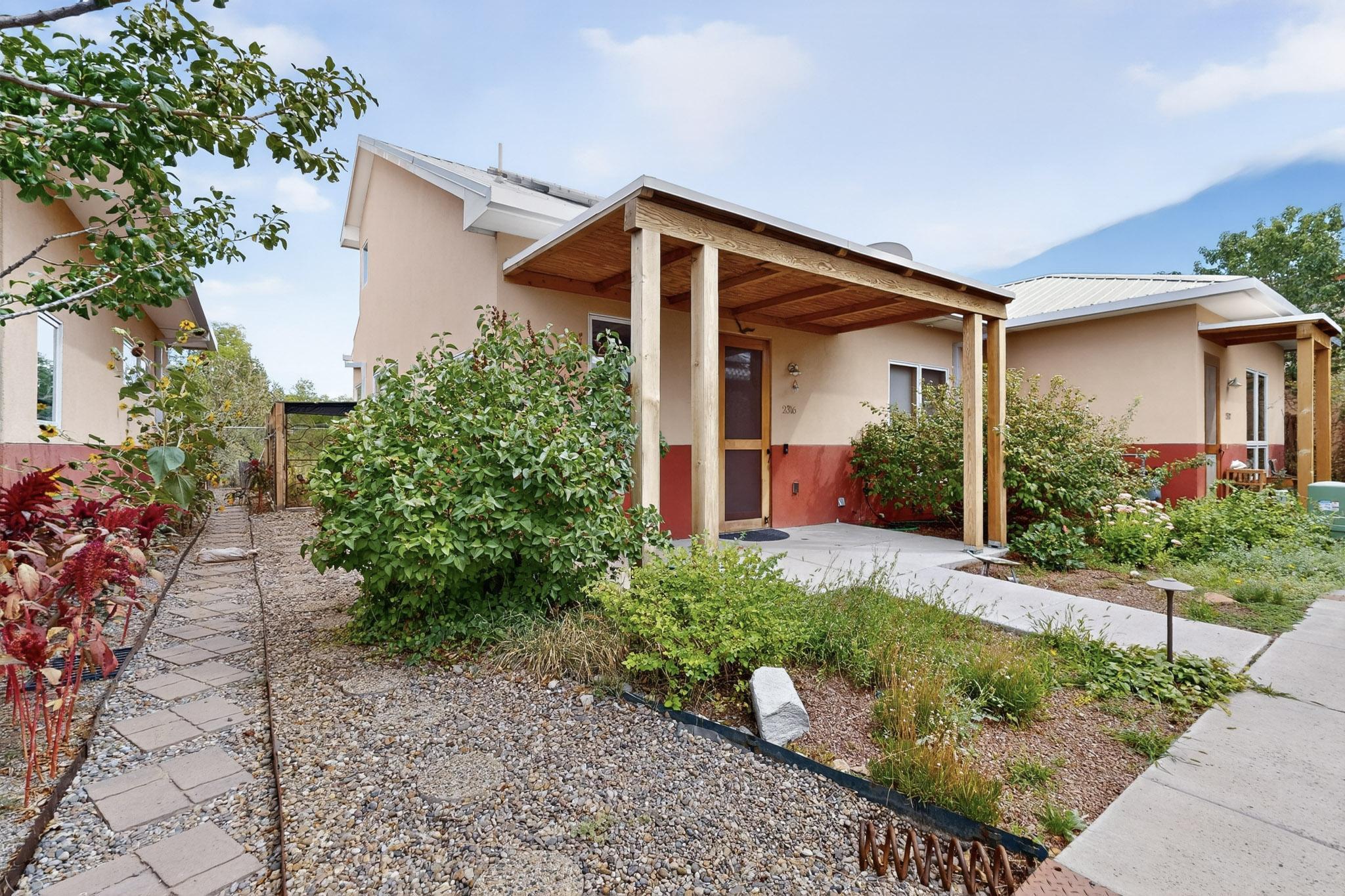 Unique co-housing development in close-knit North Valley! This move-in-ready home is perfect for low-maintenance North Valley living. Primary bedroom is downstairs. Amazing location, right off Rio Grande and steps from La Monita Coop grocery. Largest home in the community! Recent fresh Low VOC paint and carpet. A 7'' sound barrier provides additional privacy.  12 west-facing OWNED solar panels (usually $0 bill!), home irrigation system, two 90 gallon rain barrels. Meeting room , patio, & casita for members use. Casita can be reserved for guests at $30 nightly rate: includes bedroom, kitchenette, bathroom. Covered parking, secure storage, fenced backyard. Owners share the guest casita, plaza, meeting room, and gardens.