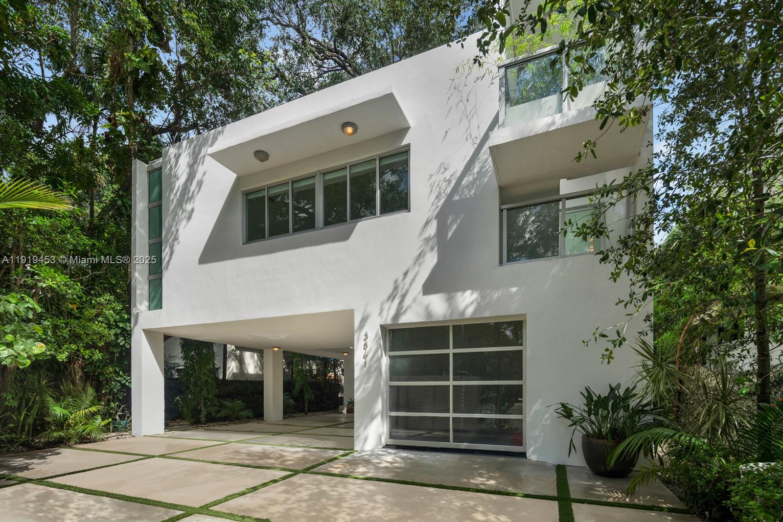 Designed by architect D.B. Lewis, this gated 2017 contemporary home in Coconut Grove offers a spacious layout ideal for entertaining. A dramatic three-story atrium greets you on entry, anchored by two mature oak trees. The lower level features a seamless indoor-outdoor flow and a chef’s kitchen with a gas Gaggenau cooktop and Miele and Viking appliances. Five en-suite bedrooms include a private primary wing with lounge, spa-style bath, and windowed walk-in closet. A 1-car air-conditioned garage and driveway space for three more vehicles add convenience. The rooftop retreat boasts a pool, gazebo, and cabana bath.