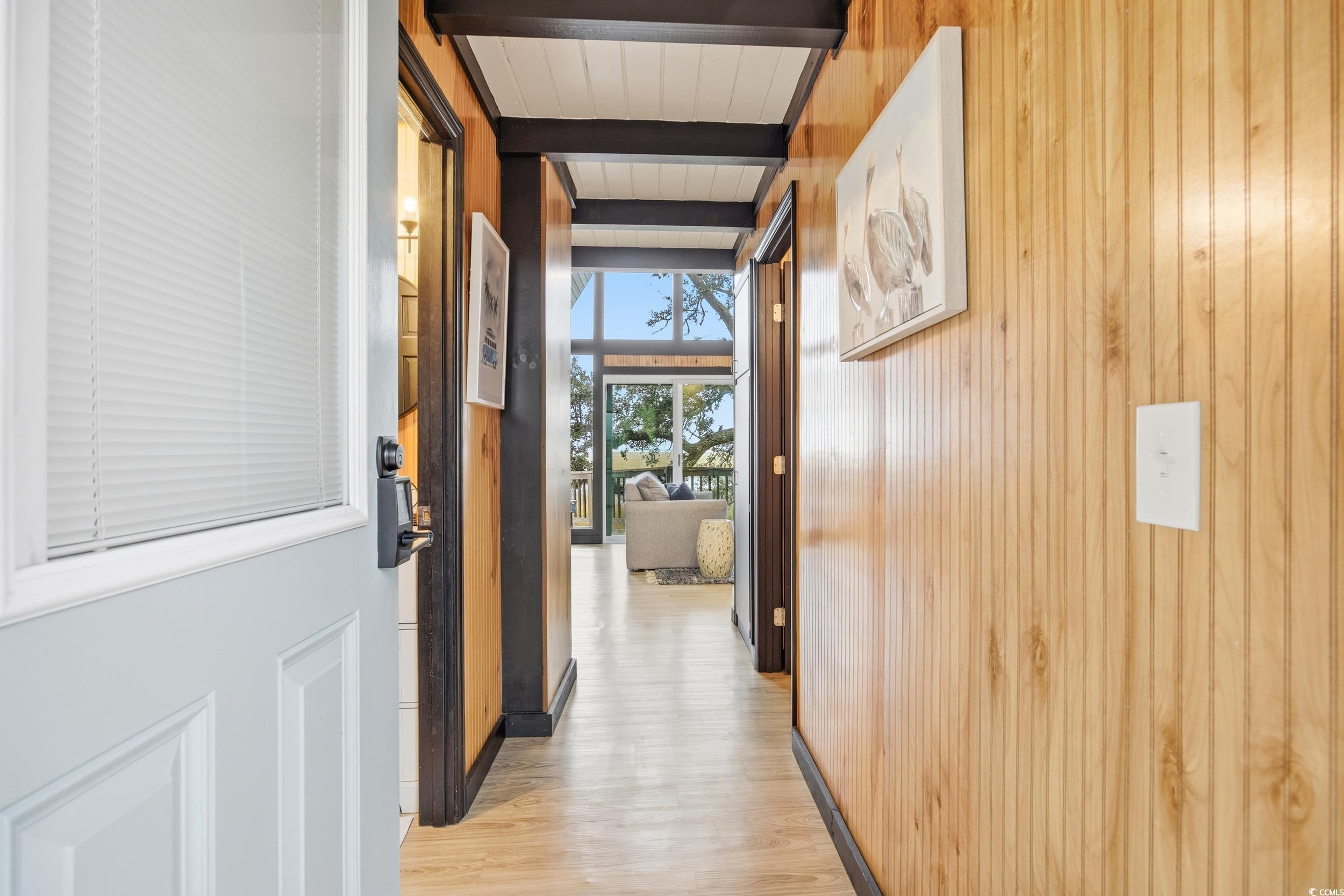 Corridor with light wood-type flooring, beam ceiling, and wood walls