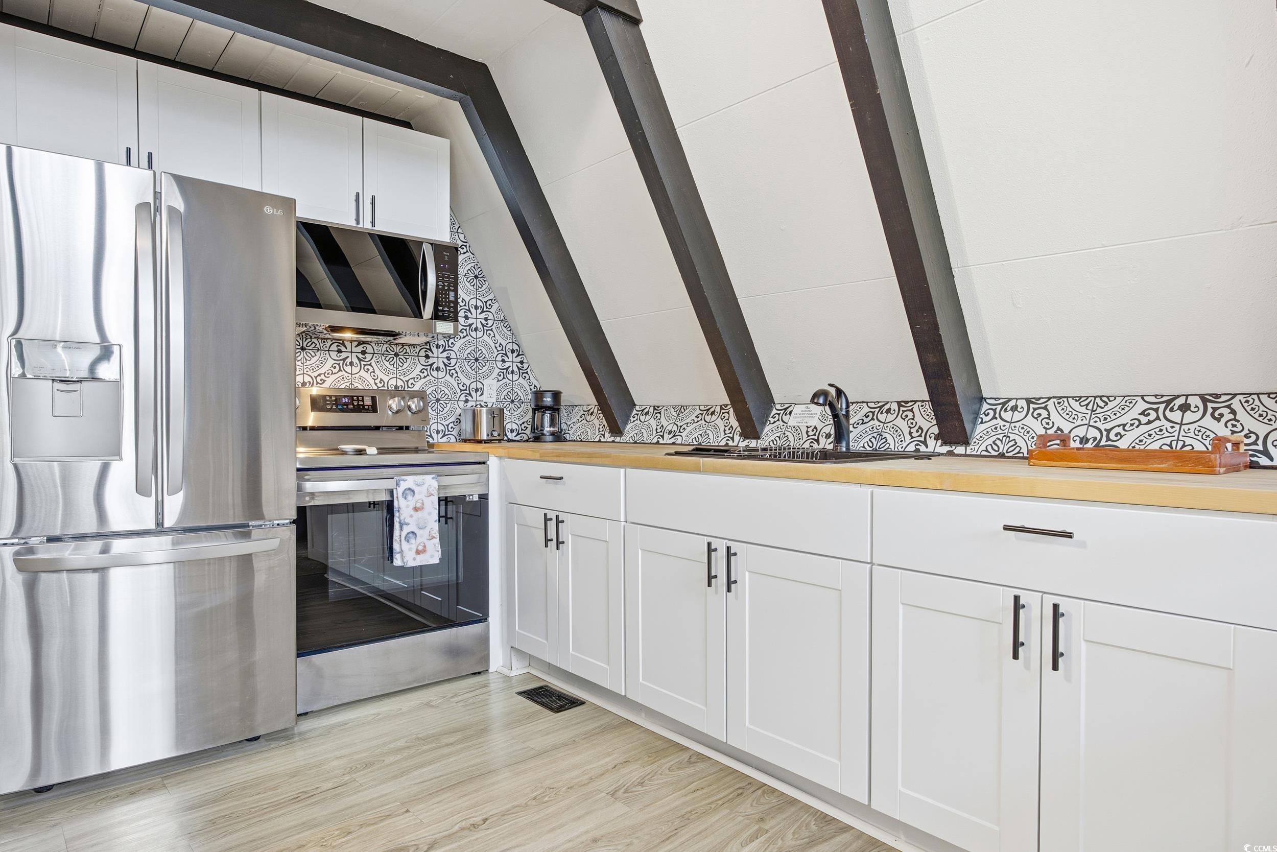 Kitchen featuring stainless steel appliances, white cabinetry, wood counters, beamed ceiling, and light wood-type flooring
