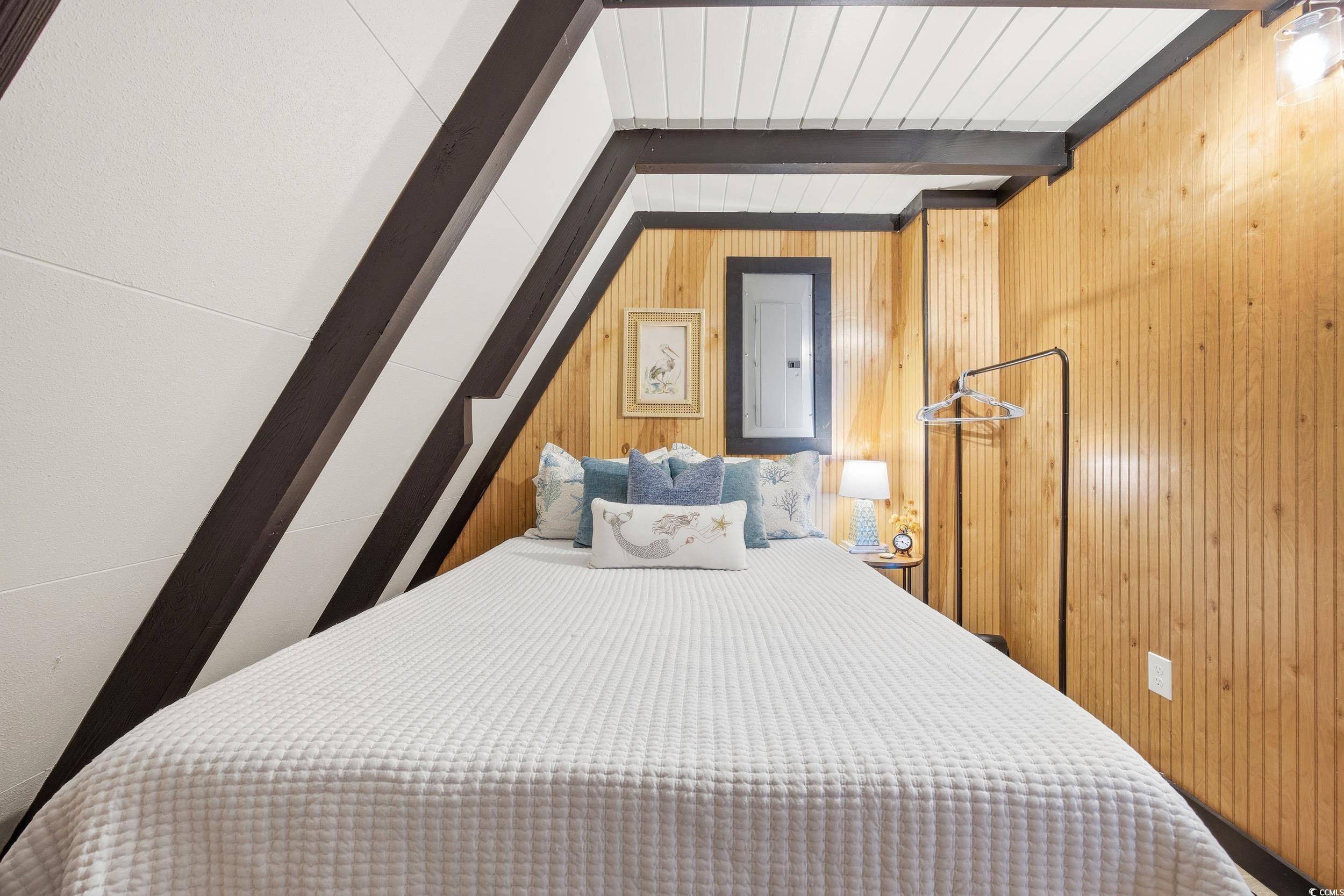 Bedroom featuring wooden walls, beamed ceiling, and electric panel