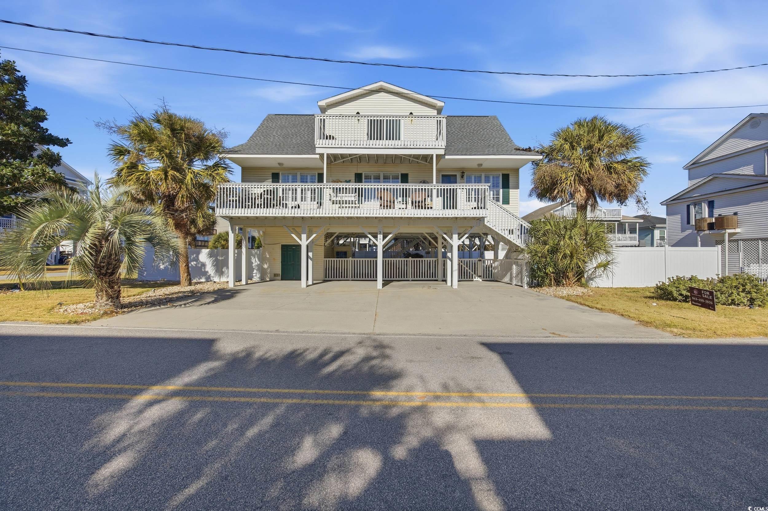 Raised beach house with a carport, concrete driveway, a balcony, roof with shingles, and stairs