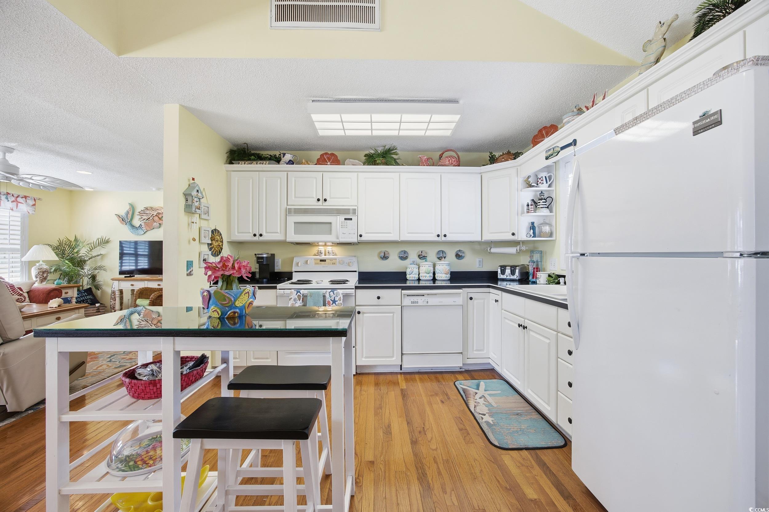 Kitchen featuring white appliances, dark countertops, white cabinetry, light wood-style flooring, and open shelves