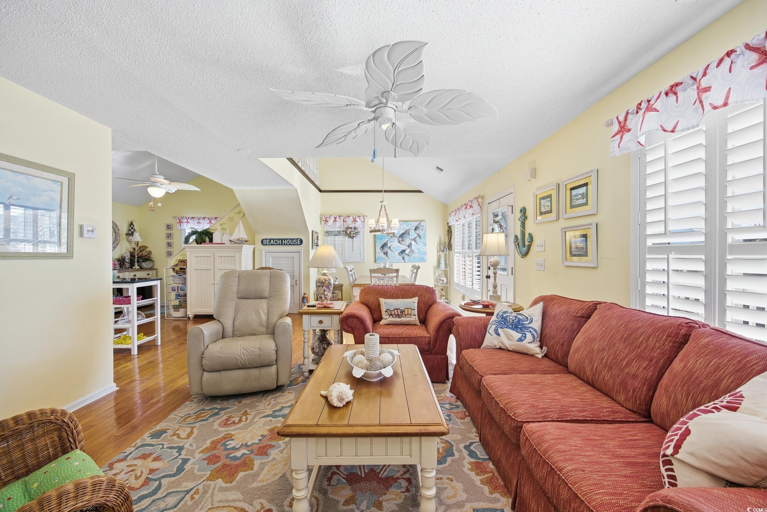 Living area featuring wood finished floors, a textured ceiling, a ceiling fan, and vaulted ceiling