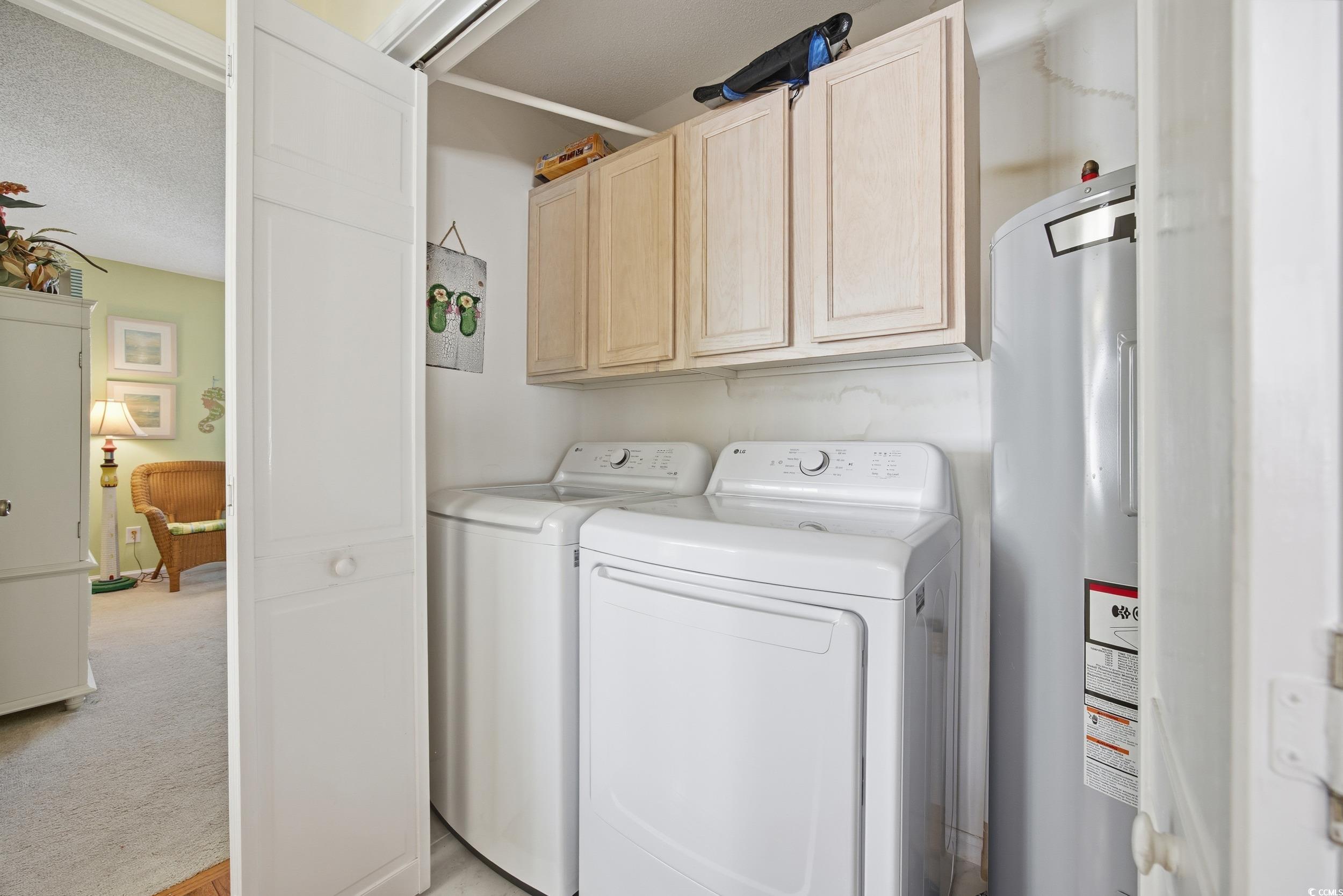 Washroom with electric water heater, cabinet space, light carpet, a textured ceiling, and washing machine and dryer