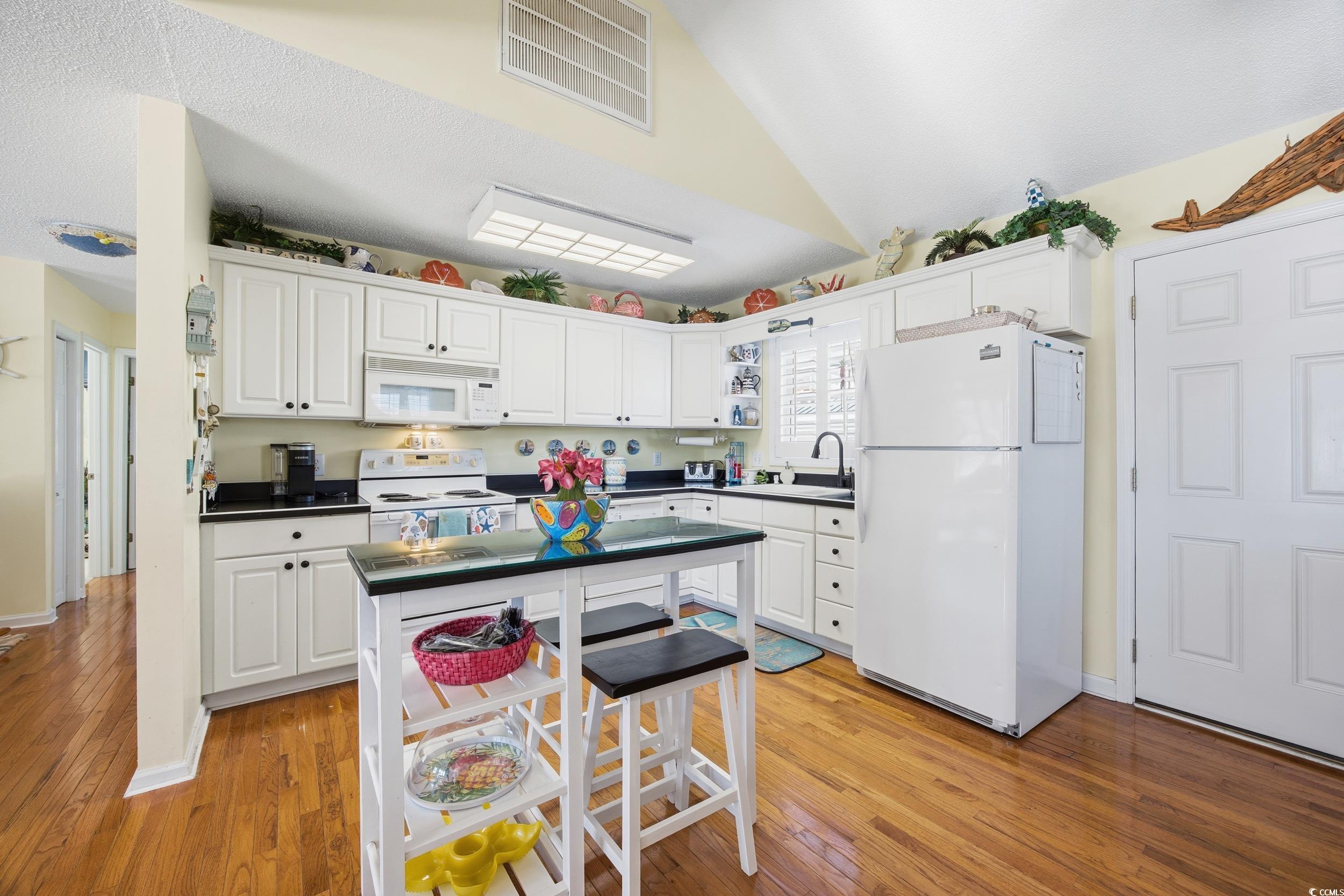 Kitchen featuring white appliances, white cabinets, lofted ceiling, dark countertops, and light wood finished floors