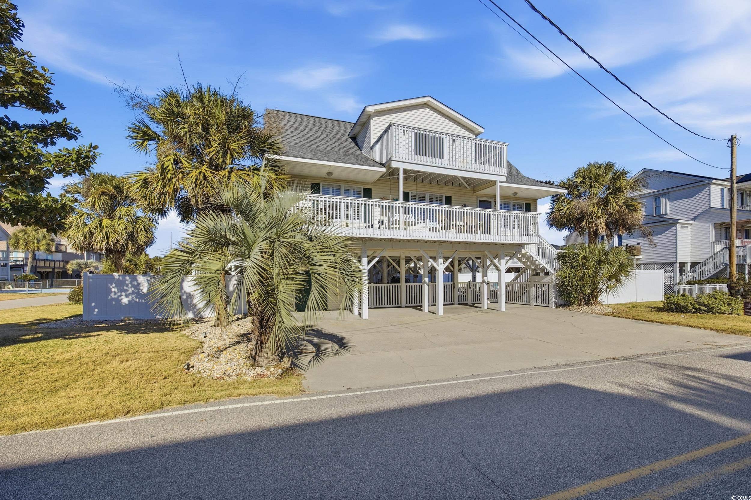 Beach home with a carport, roof with shingles, driveway, a balcony, and stairway